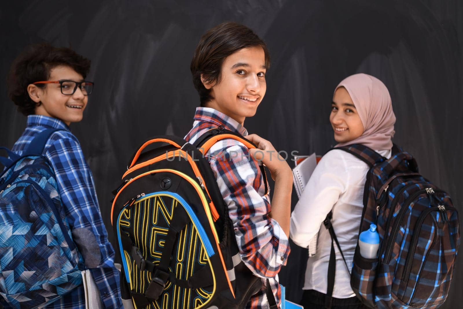 Arabic teenagers, students group portrait against black chalkboard wearing backpack and books in school.Selective focus  by dotshock