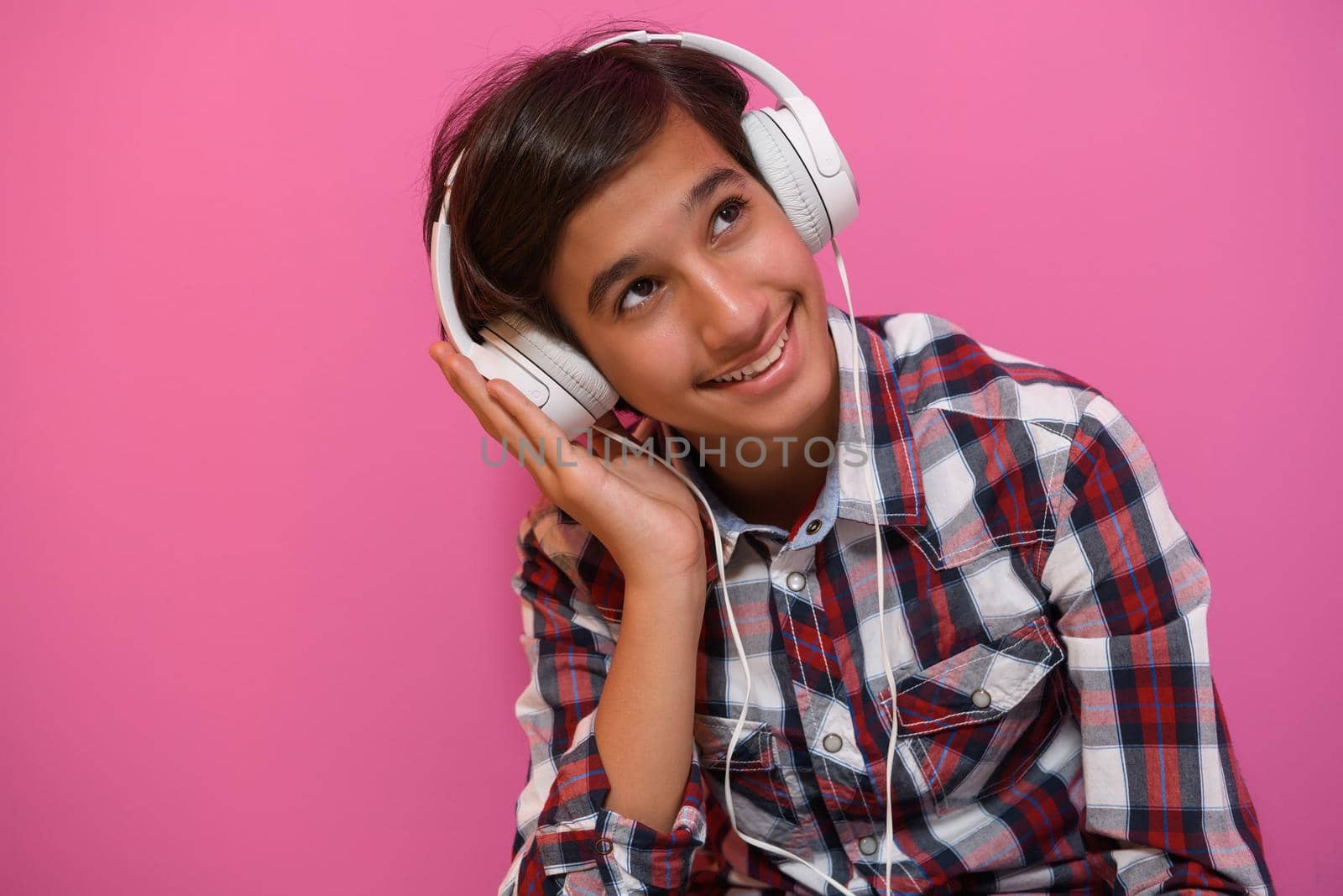 Arabic Teenage Boy Wearing Headphones And Listening To Music pink background. High quality photo