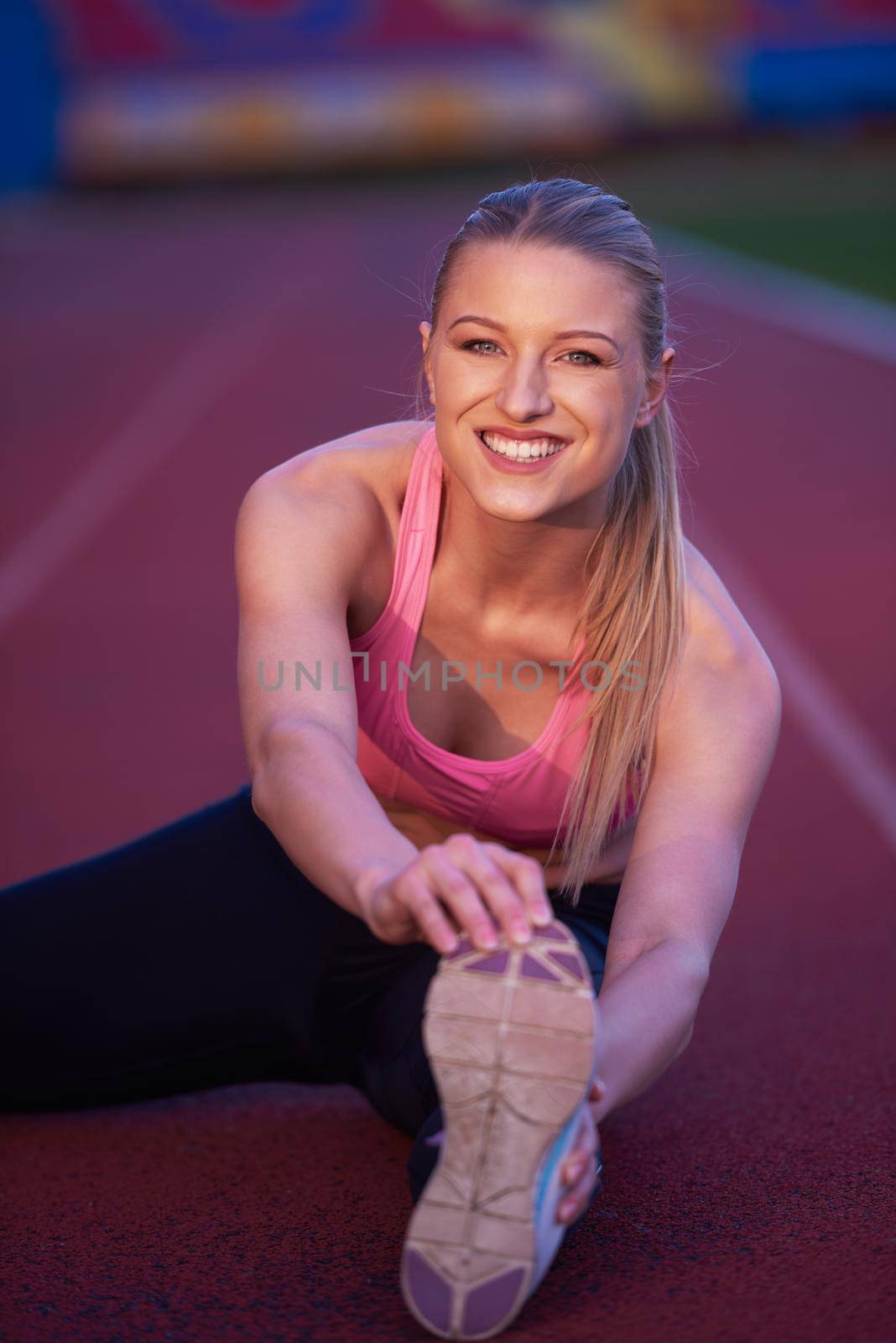 young runner sporty woman relaxing and stretching on athletic race track