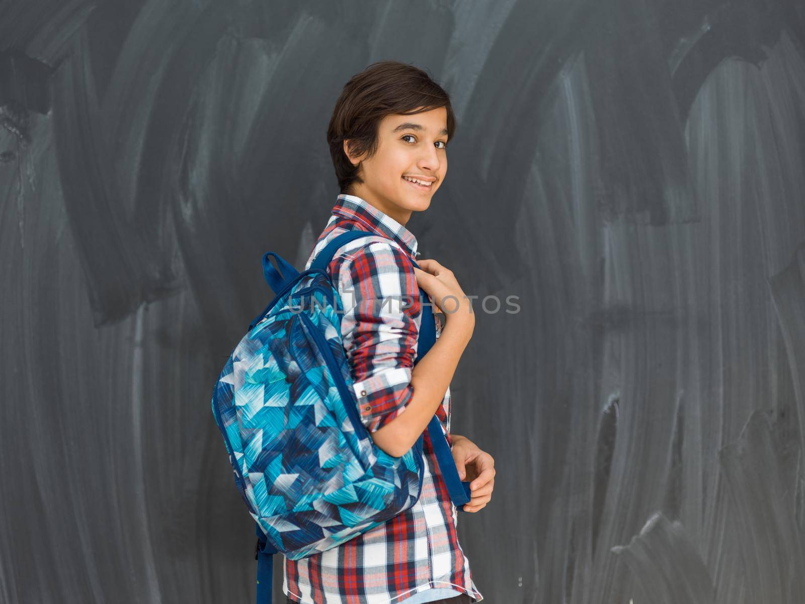 Arab teenager with backpack wearing casual school look against a black chalkboard background. High quality photo