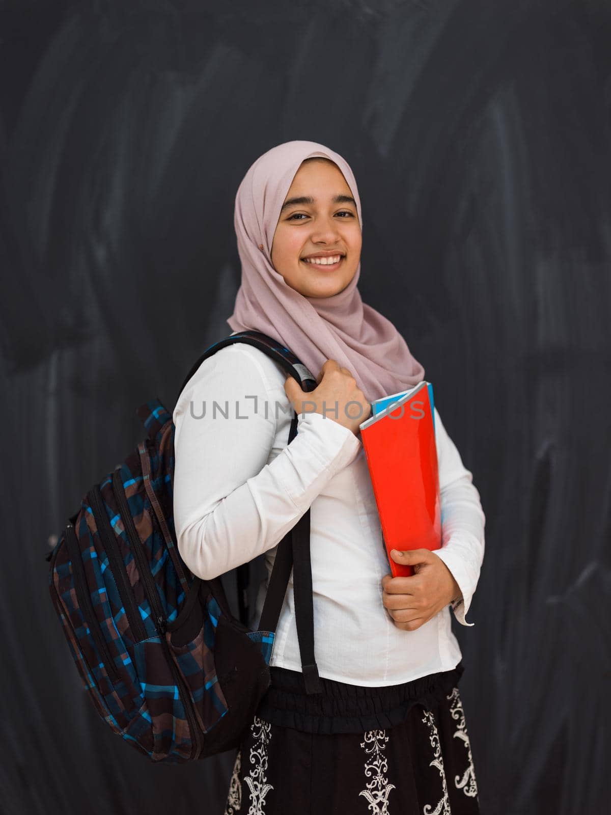 portrait of happy female middle eastern university student against black chalkboard in classroom by dotshock