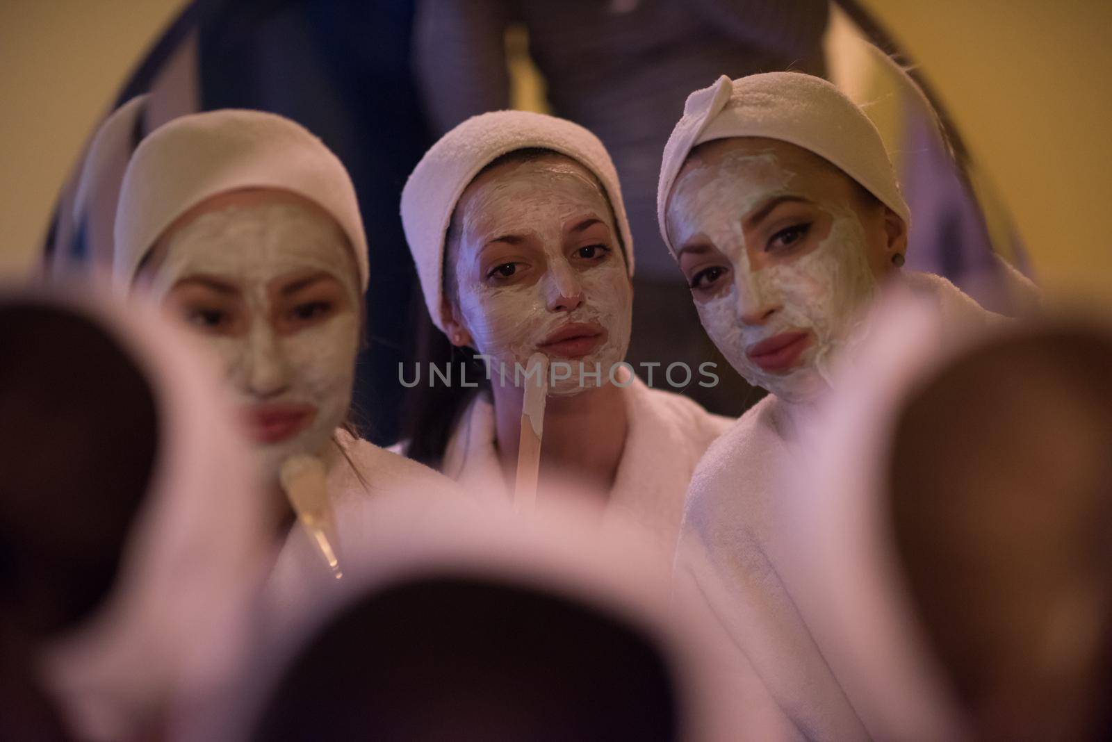 a group of young beautiful women looking in the mirror while putting face masks in the bathroom