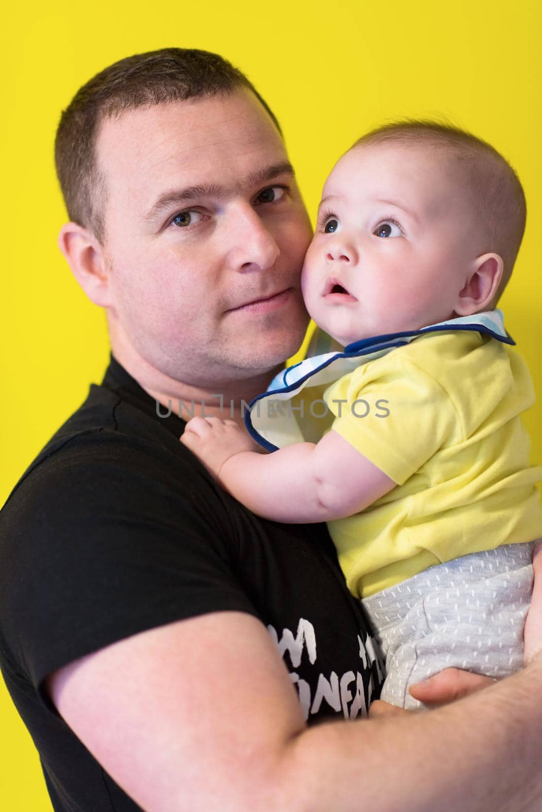 portrait of happy young father holding baby isolated on yellow by dotshock