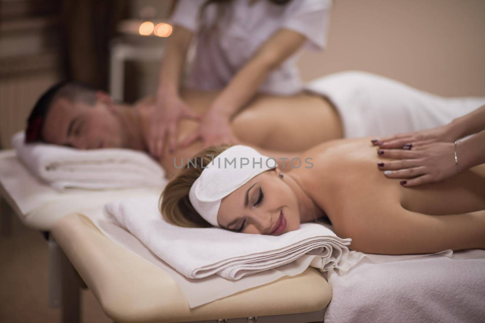 Relaxed young beautiful couple receiving a back massage from masseur in a spa