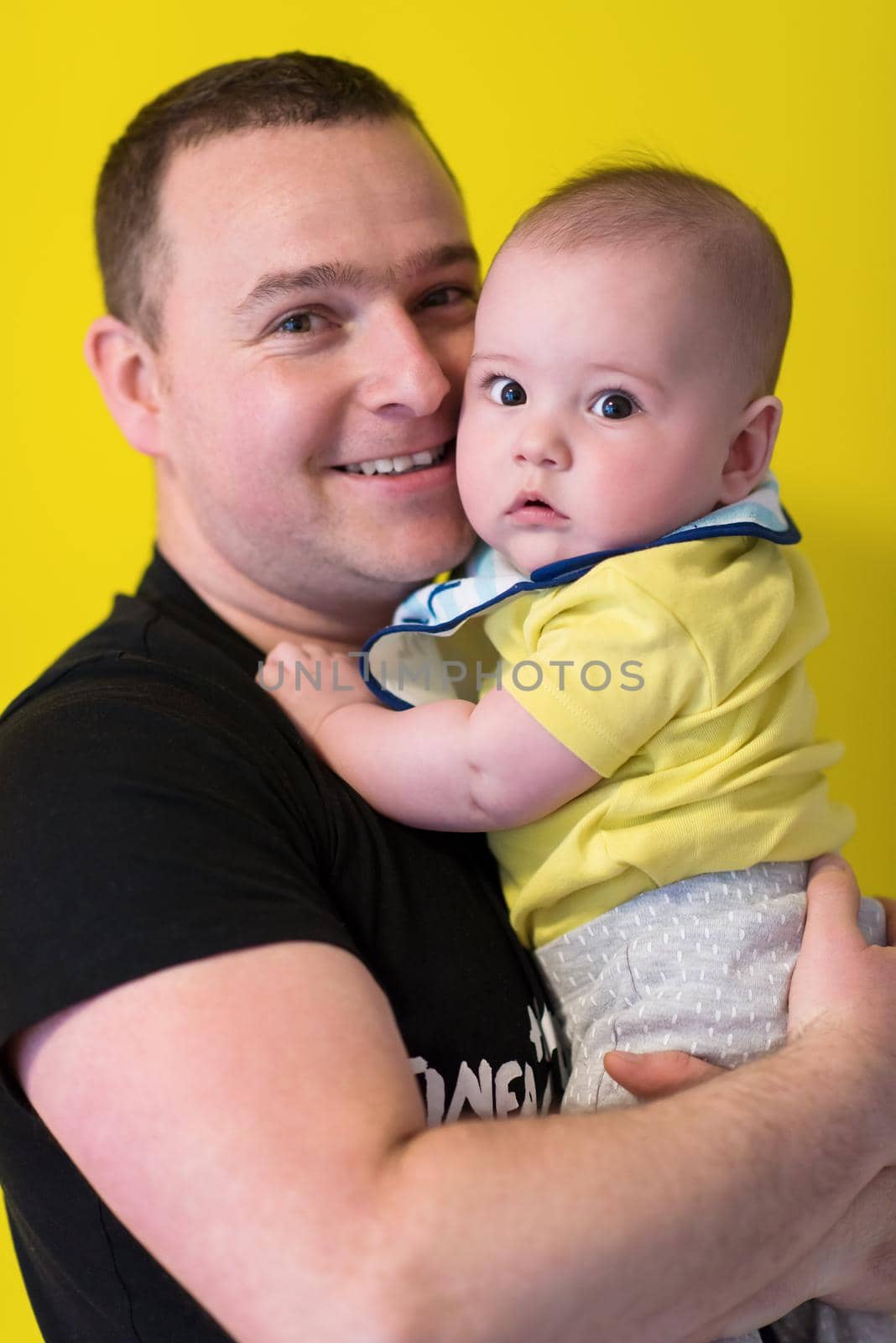 portrait of happy young father holding baby isolated on yellow by dotshock