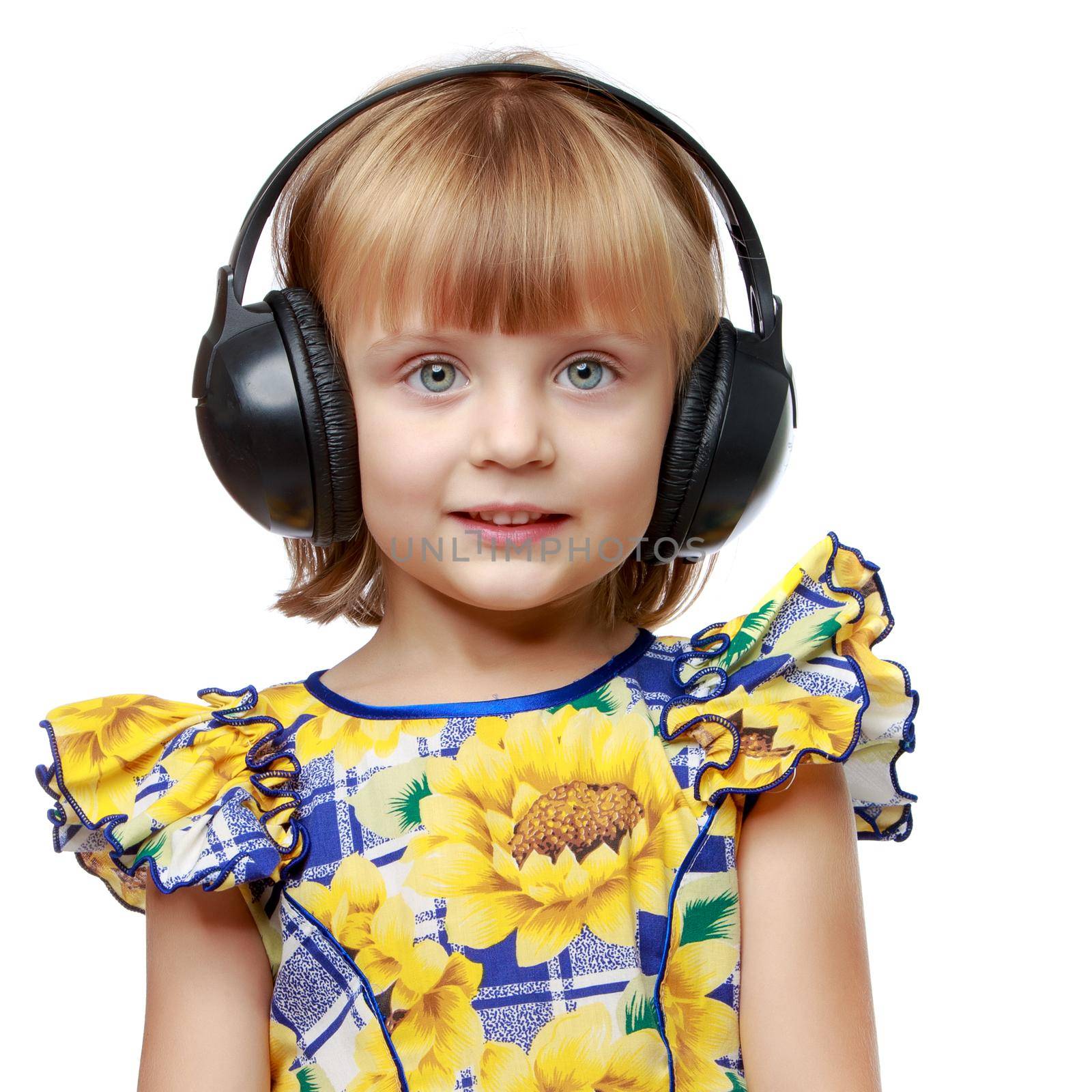 Beautiful little girl listening to music through large stereo headphones. The concept of musical education, advertising of musical goods, CDs of various performers. Isolated on white background.