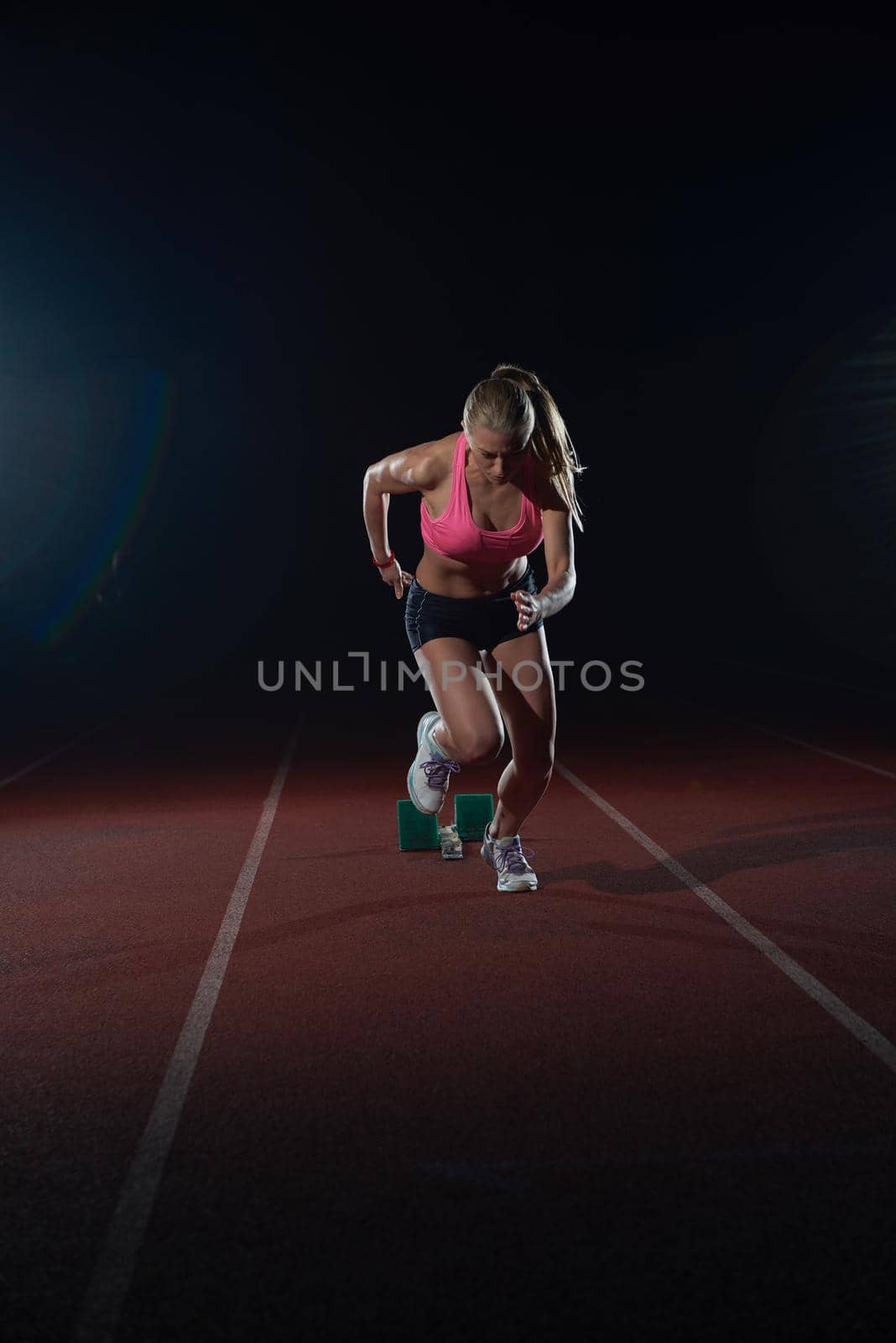 woman  sprinter leaving starting blocks on the athletic  track. Side view. exploding start