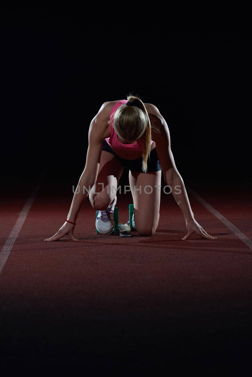 woman  sprinter leaving starting blocks on the athletic  track. Side view. exploding start