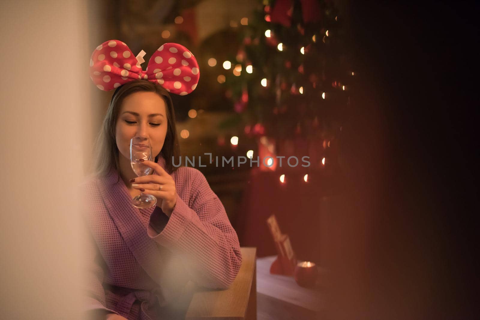 people, and relaxation concept   beautiful young woman in bath robe drinking champagne at spa over holidays lights background