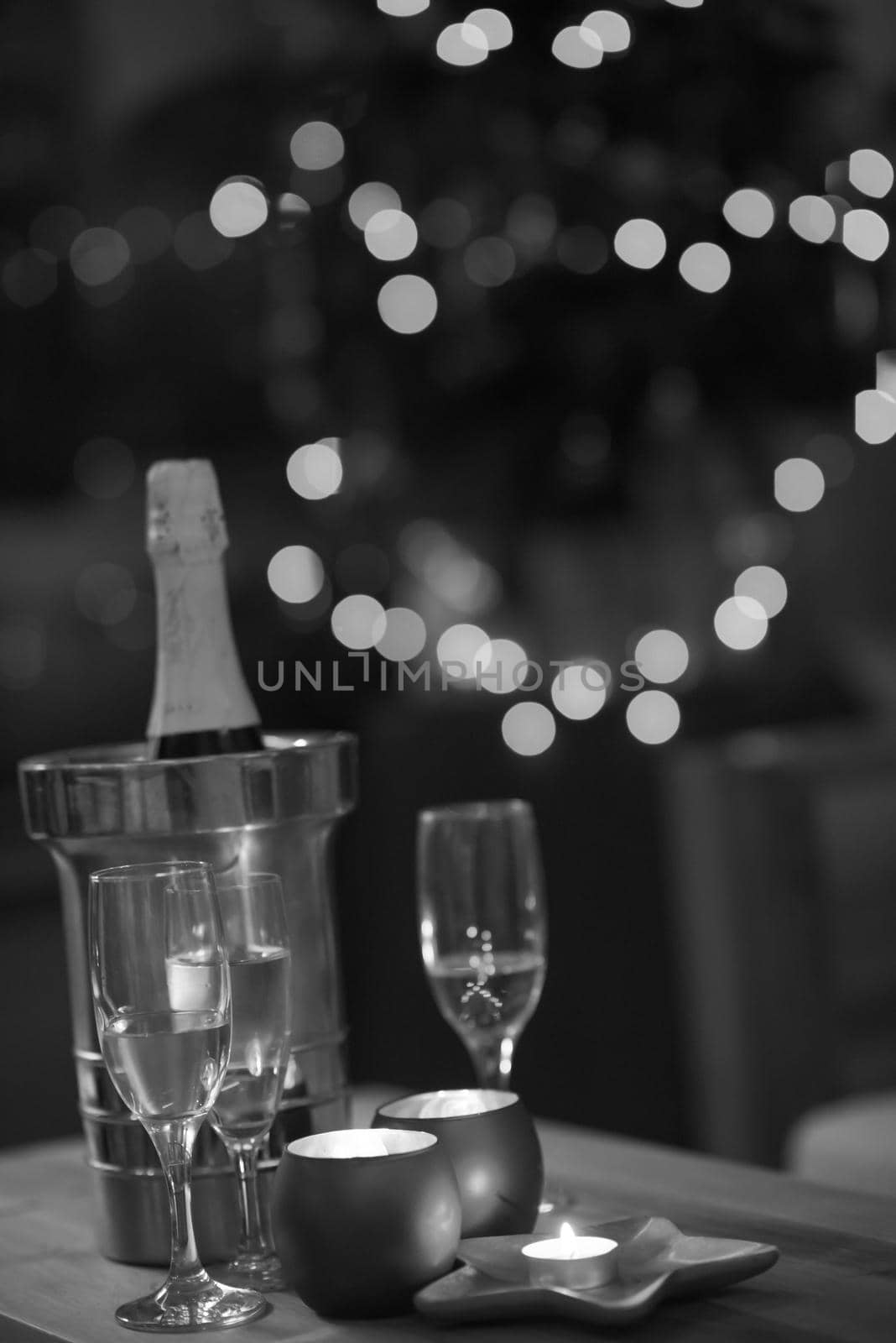 champagne and crystal glasses on a wooden table with candles and holiday lights in the background