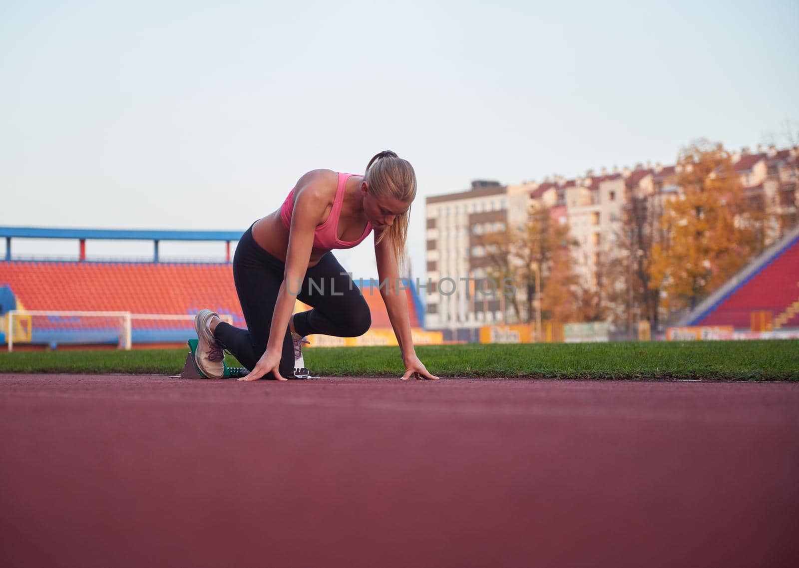 woman  sprinter leaving starting blocks on the athletic  track. Side view. exploding start