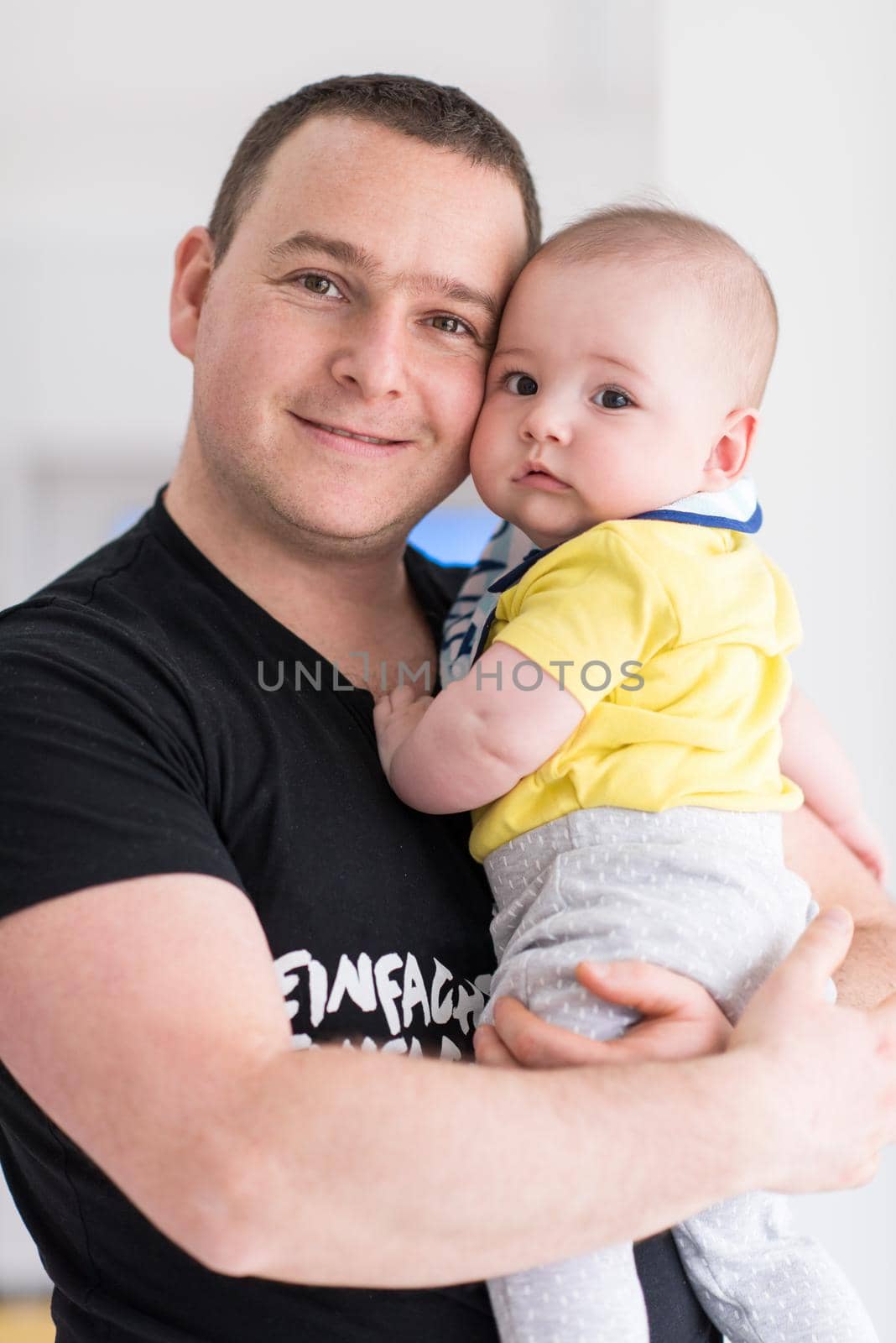 portrait of happy young father holding newborn baby boy near the window at home