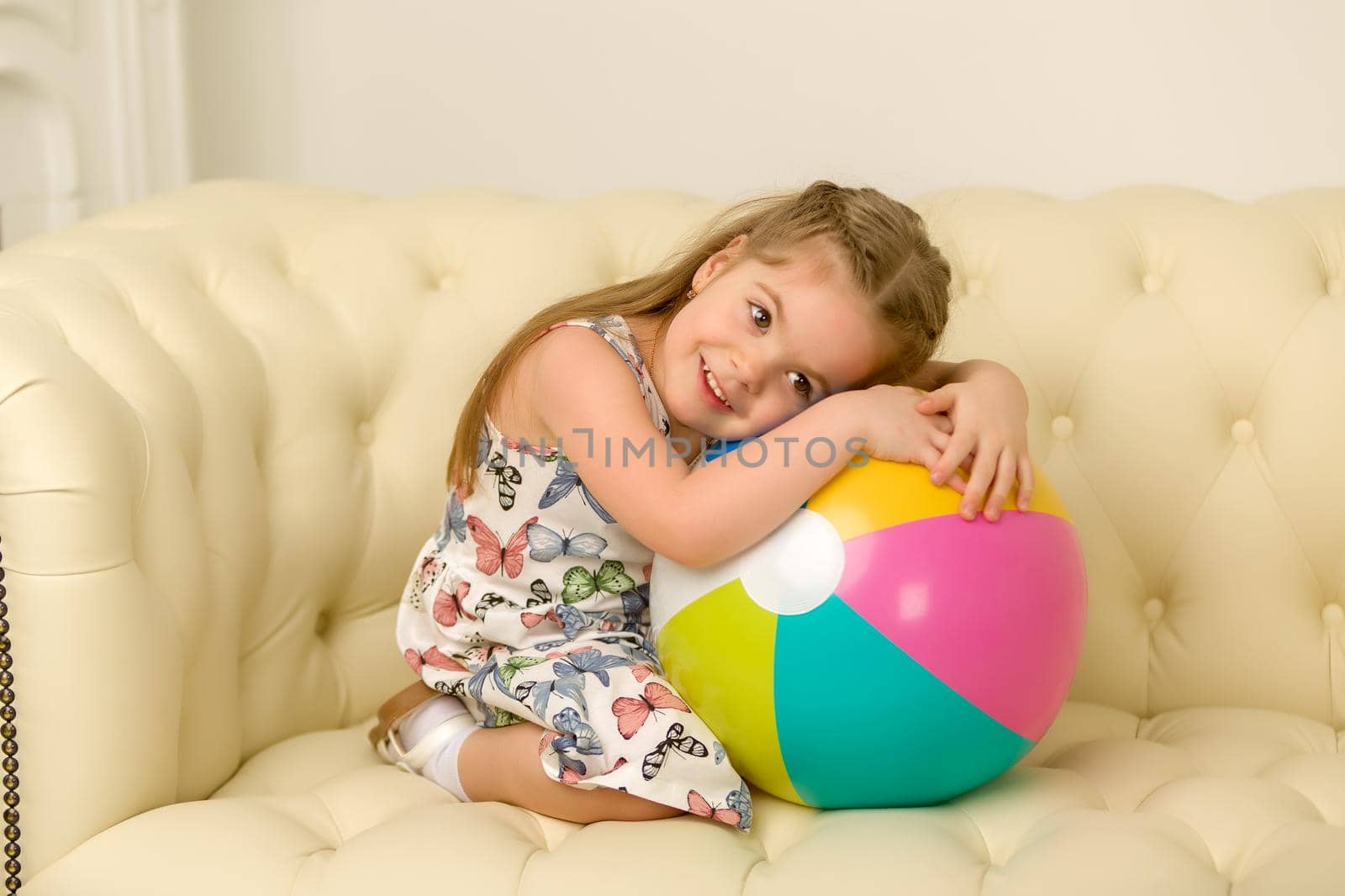 Adorable little girl playing with a ball on the sofa. Concept for family, advertising, happy childhood.