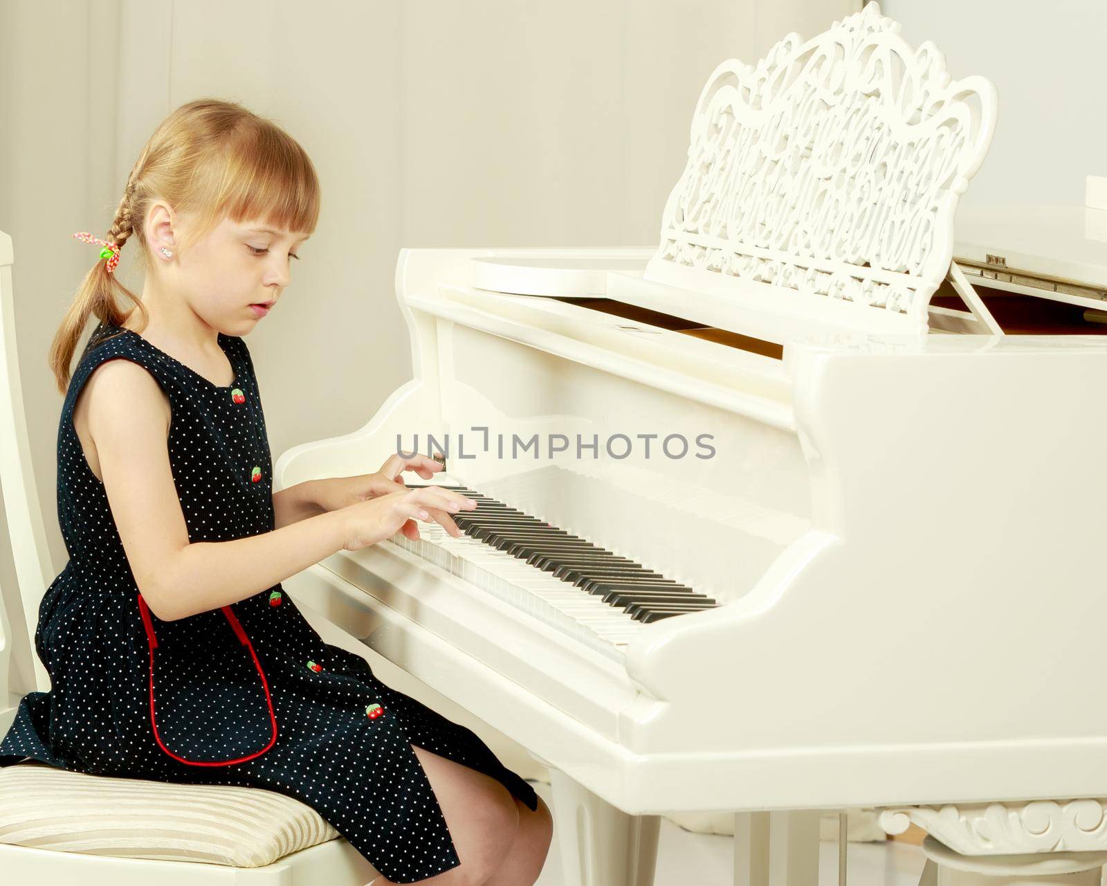 A nice little girl is playing on a big white piano. The concept of musical and aesthetic education of a child.