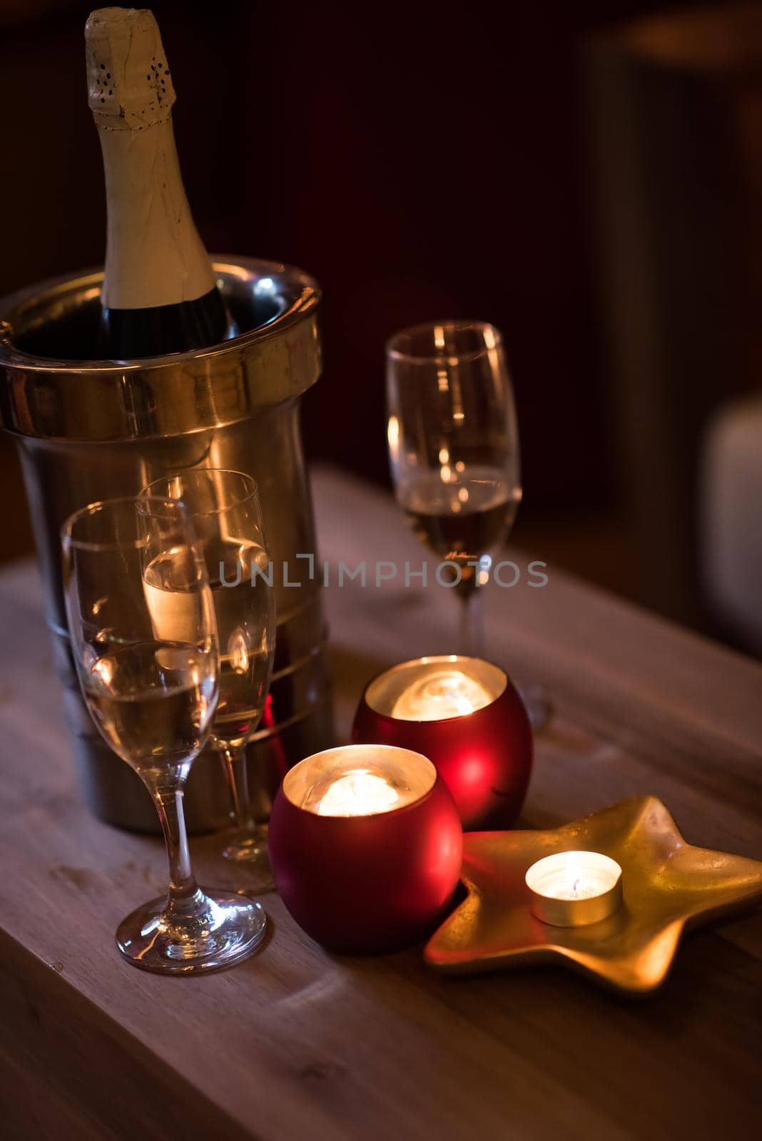 champagne and crystal glasses on a wooden table with candles and holiday lights in the background