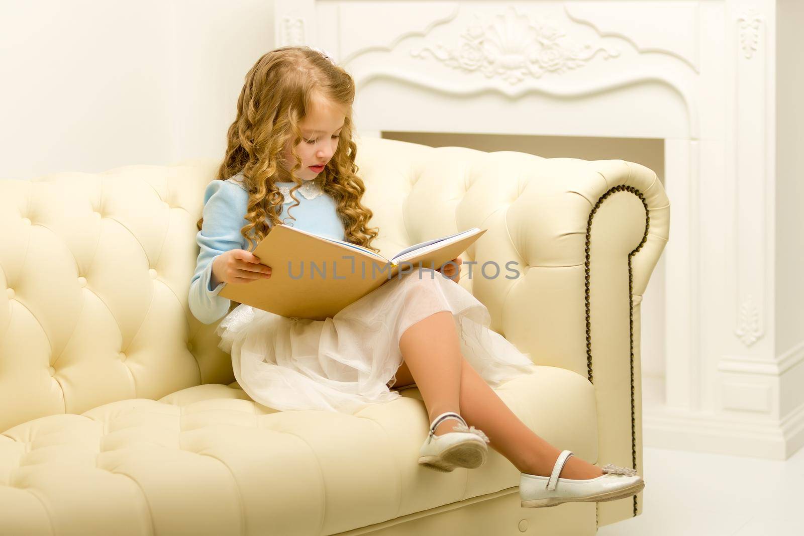 Little girl is sitting on the couch in the room. The concept of a happy childhood.