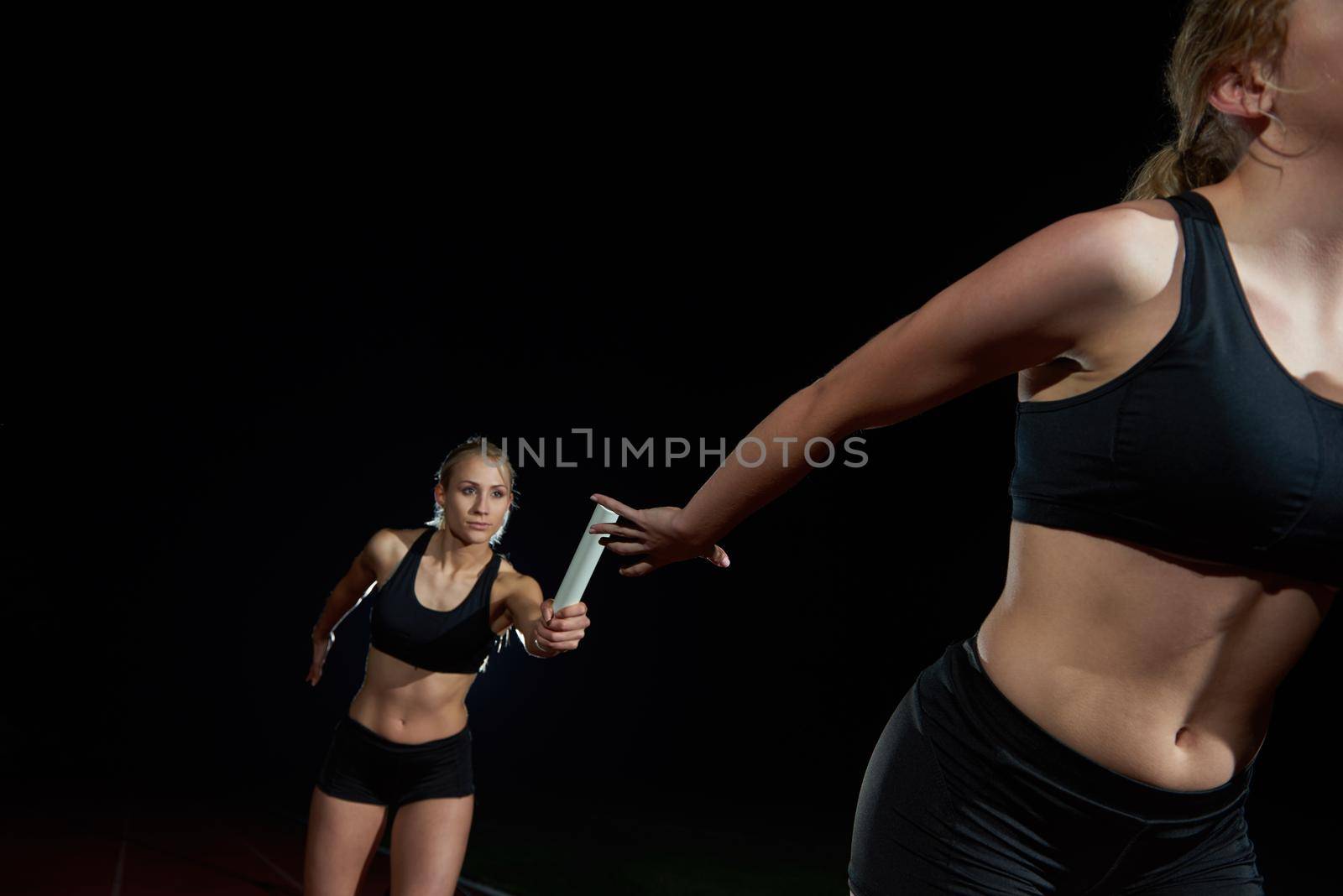 woman athletic runners passing baton in relay race