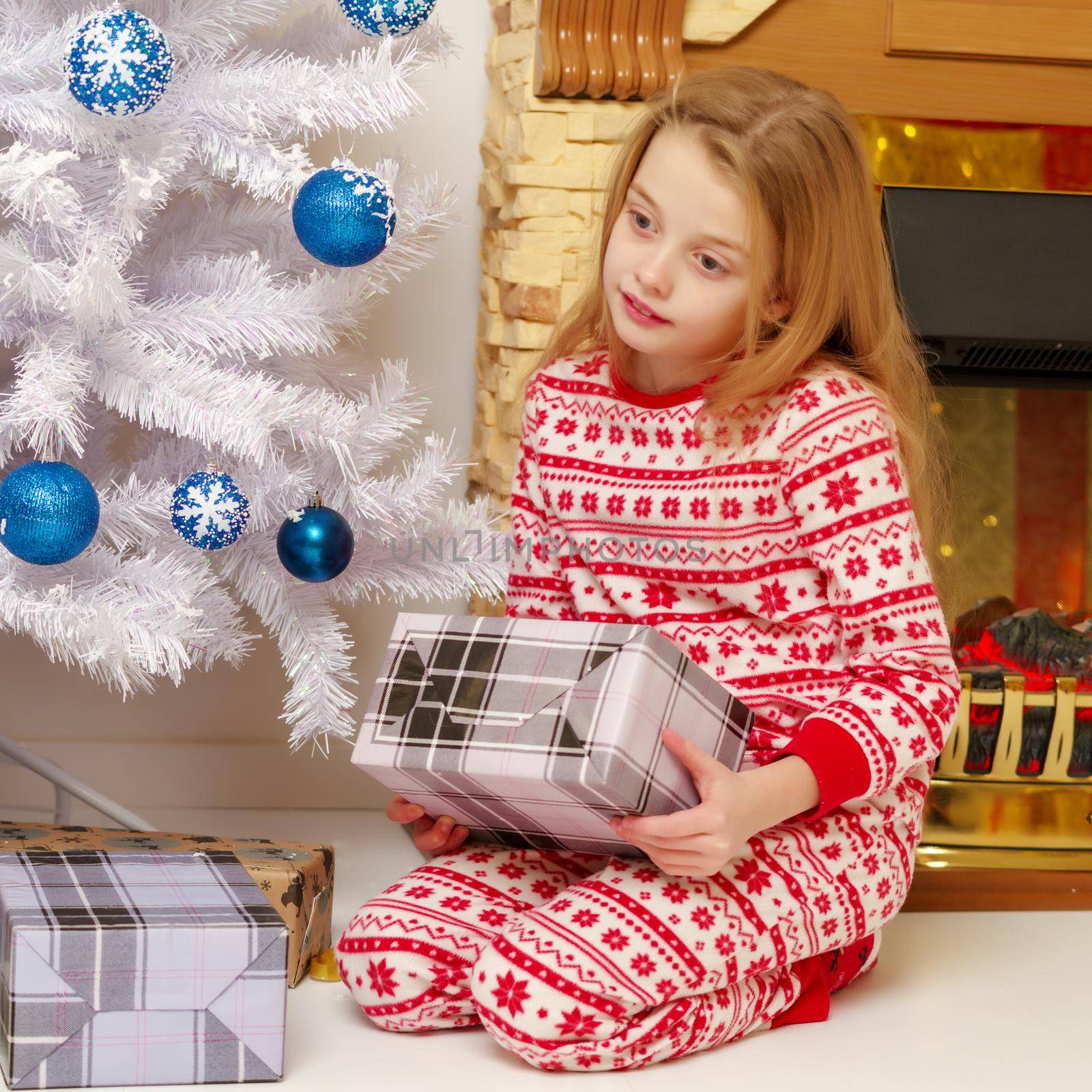 Cute little girl near the Christmas tree with a gift, studio photo. The concept of the new year, family holiday.