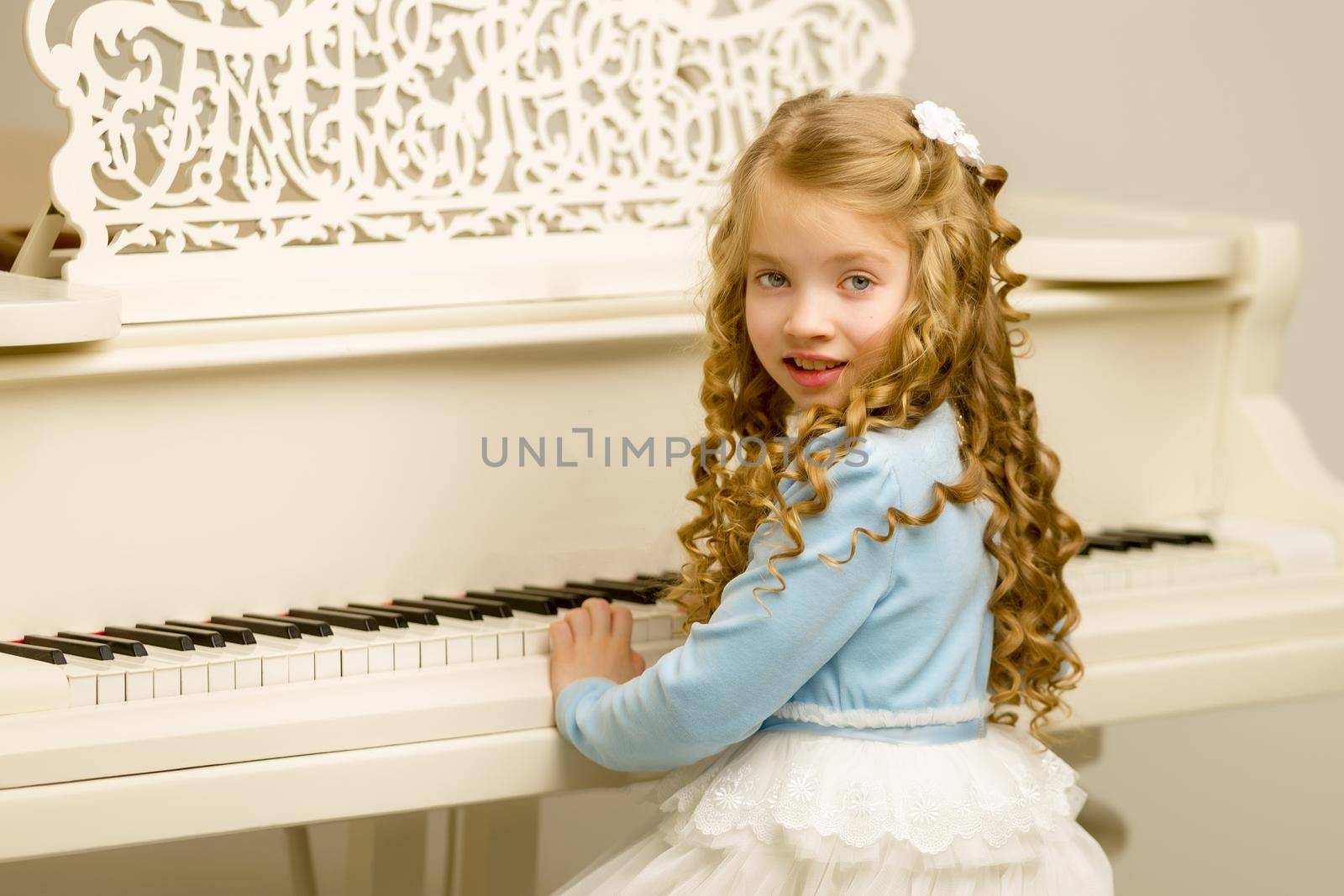 A nice little girl is playing on a big white piano. The concept of musical and aesthetic education of a child.