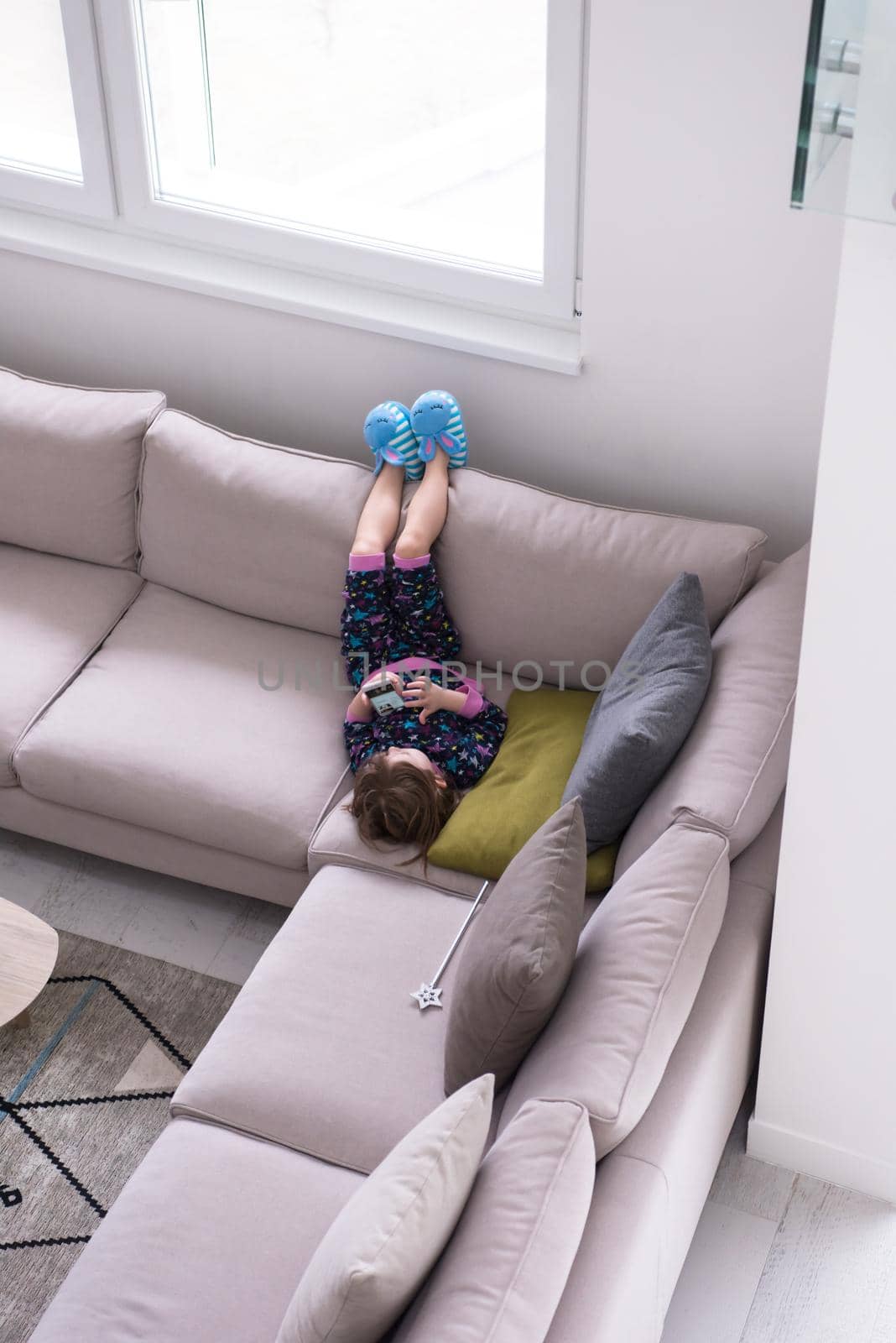 Cute little girl using a smartphone and smiling while lying on the sofa at home