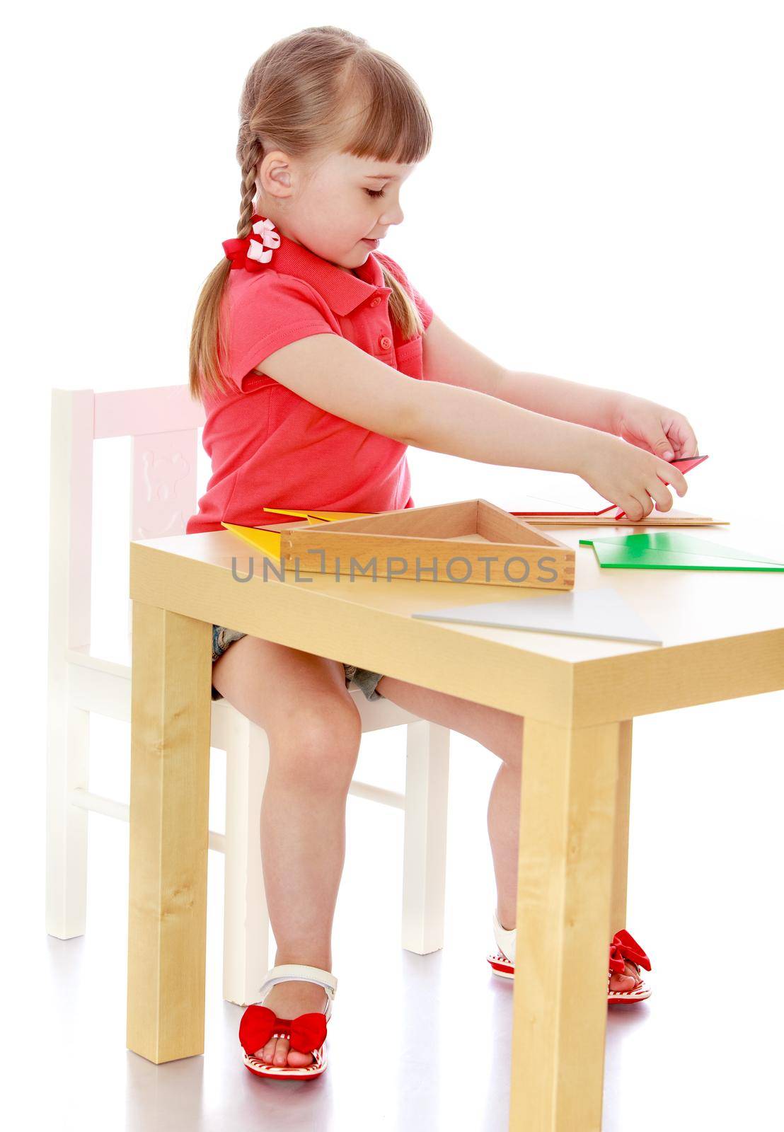 Cute little girl sitting at a table in a Montessori kindergarten. The girl works with Montessori material-Isolated on white background