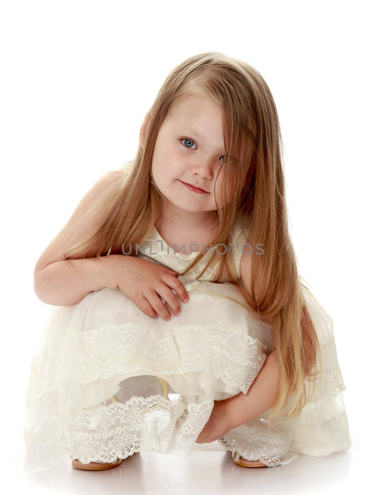 Lovely little round-faced girl with long, blonde hair below the shoulders, in a white dress. The girl squatted - Isolated on white background
