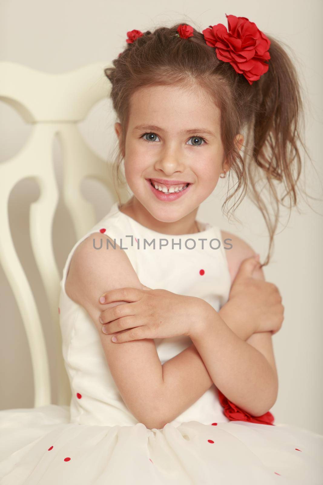 Cute little girl in white dress sitting on a white chair