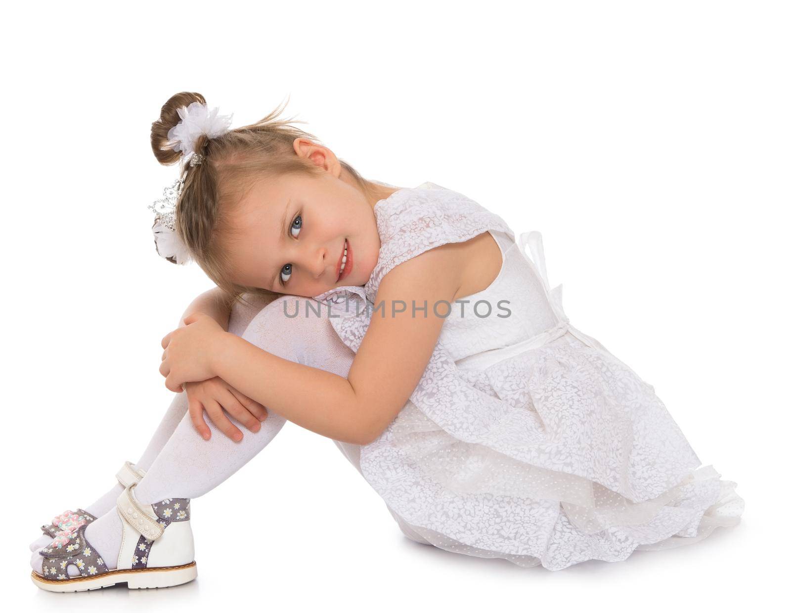 Gentle little Princess in a magnificent white dress. Girl sitting on the floor, hands folded on his knees . Looking at the camera a happy look - Isolated on white background