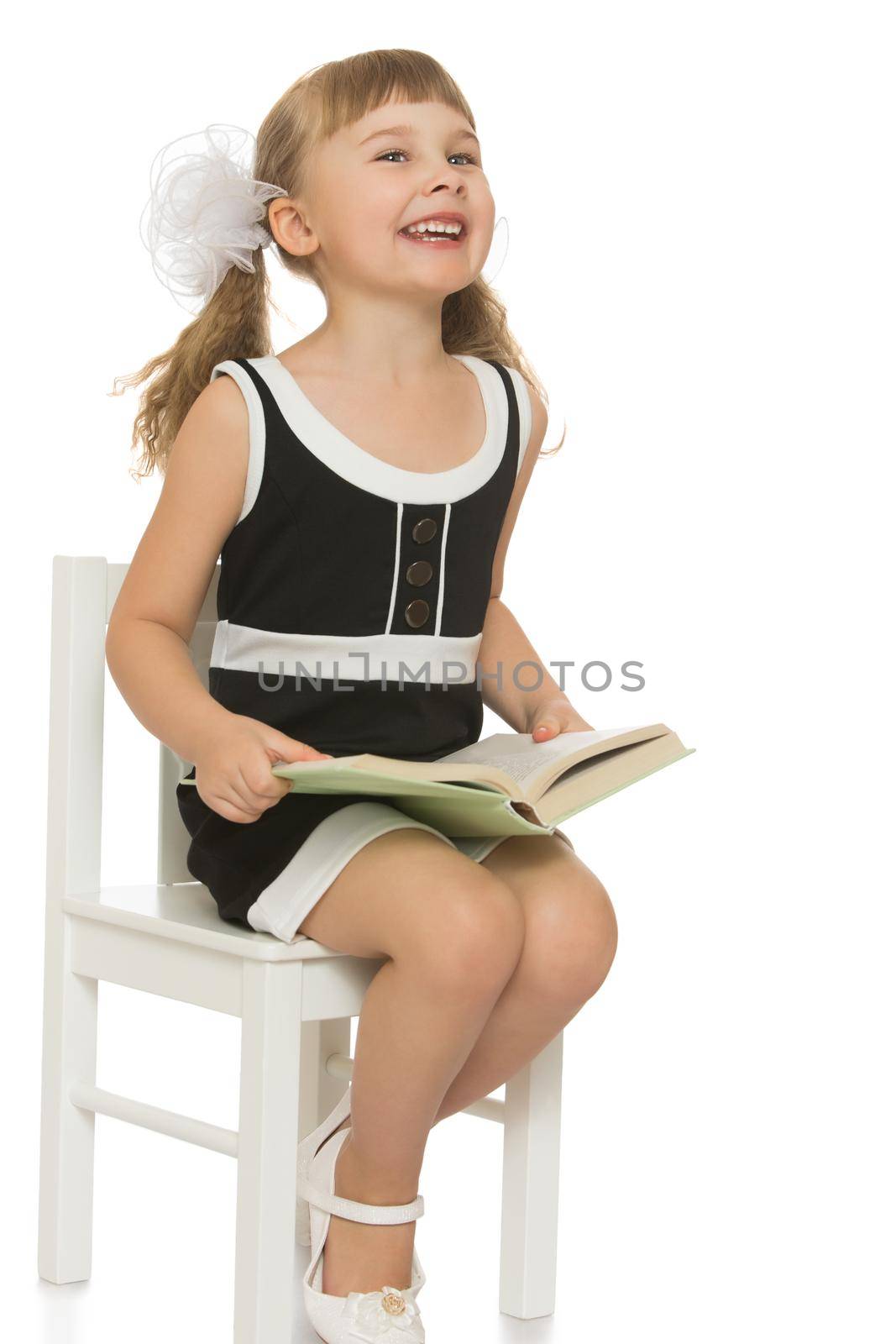 Honey girl school girl in a black dress with a book in his hands. With a white bow on her head. Sitting on a chair - Isolated on white background
