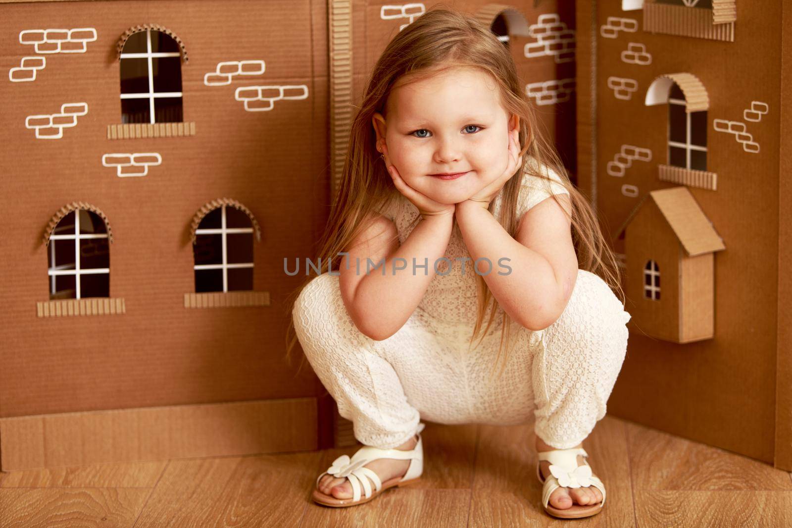 Beautiful little girl with long blond hair below the shoulders , in white dress plays with a doll's house