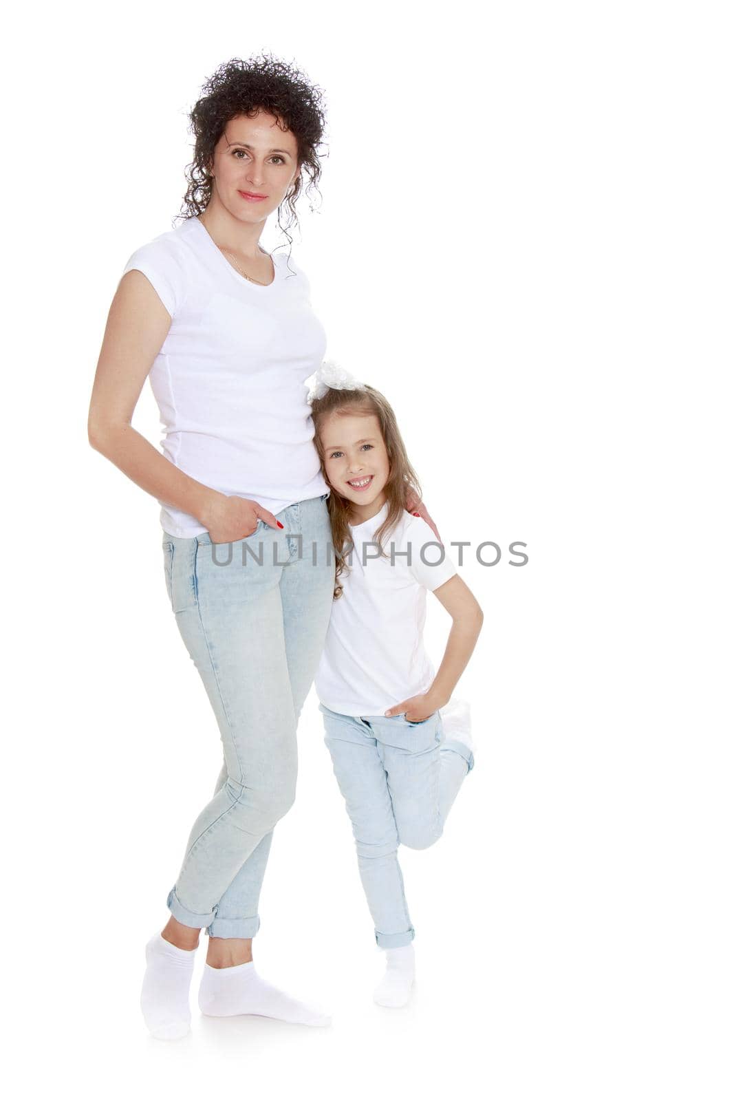 Beautiful, charming young mother with adorable little daughter. In the same jeans and white t-shirts without a pattern. Mom keeps daughter's hand - Isolated on white background