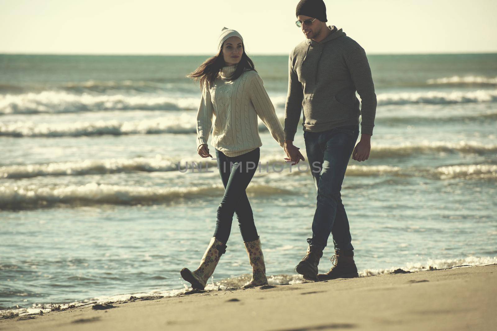 Young couple having fun walking and hugging on beach during autumn sunny day