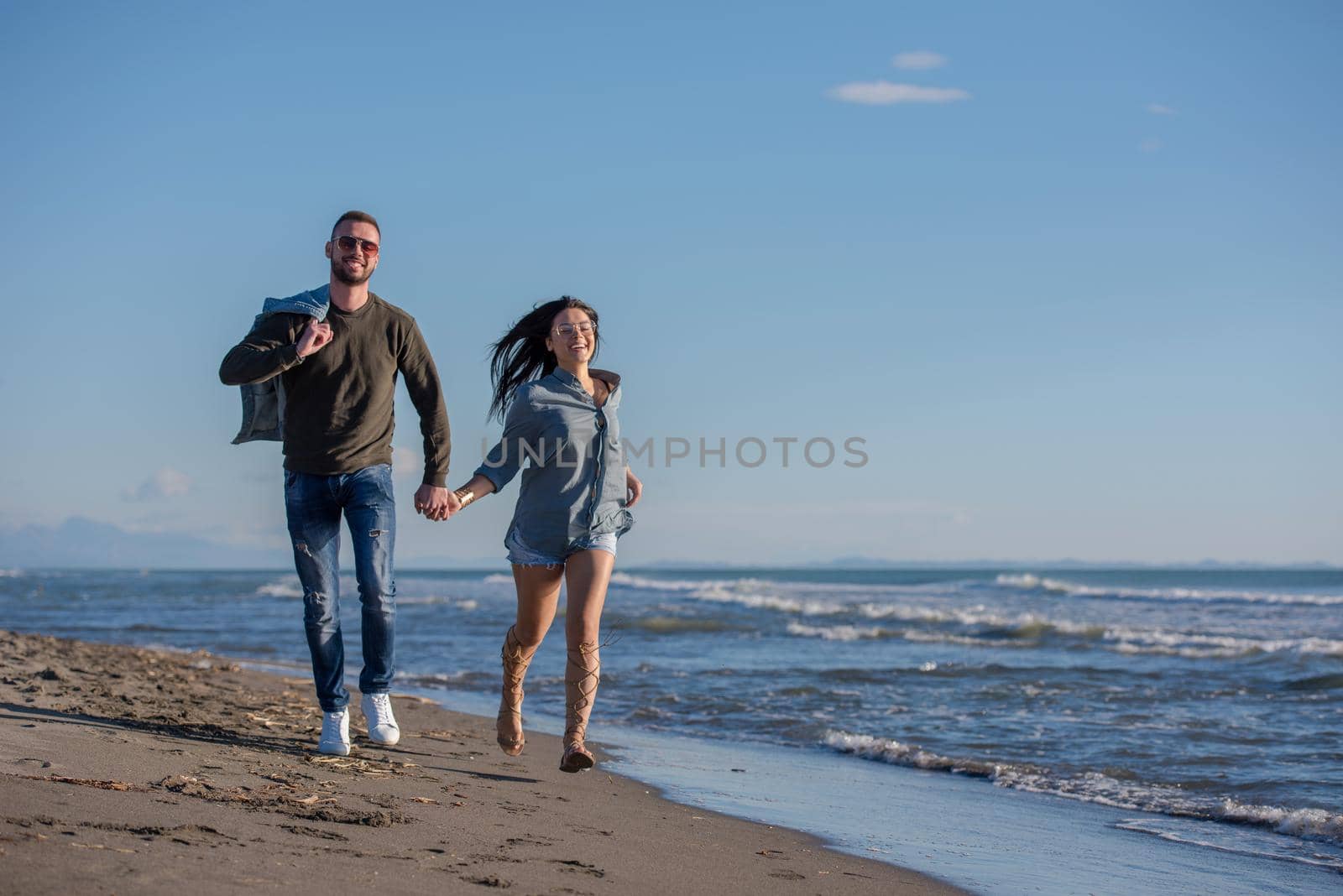 Young couple having fun walking and hugging on beach during autumn sunny day