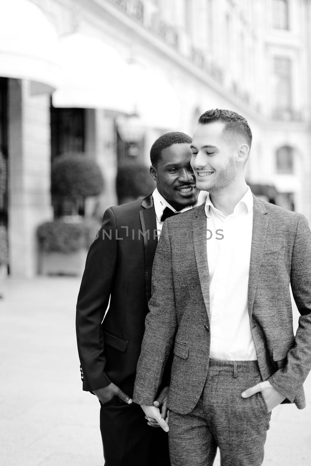 Black and white photo of afro american handsome man hugging european boy wearing suit. Concept of gays and same sex couple.