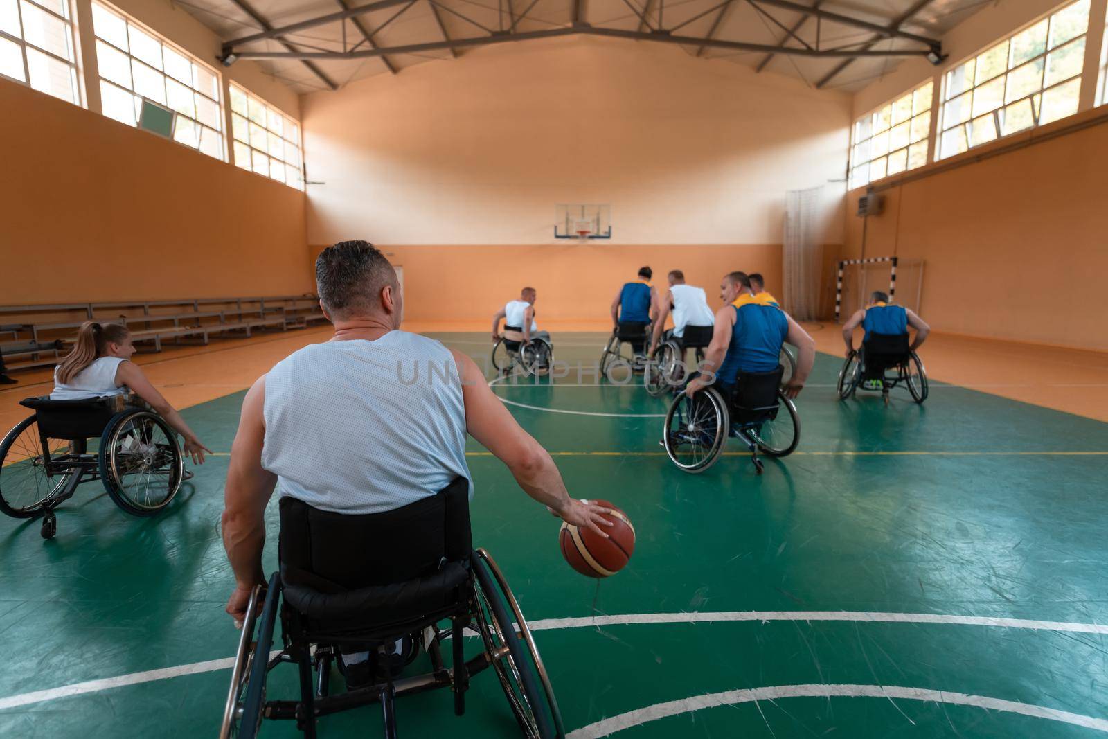 Disabled War veterans mixed race and age basketball teams in wheelchairs playing a training match in a sports gym hall. Handicapped people rehabilitation and inclusion concept by dotshock