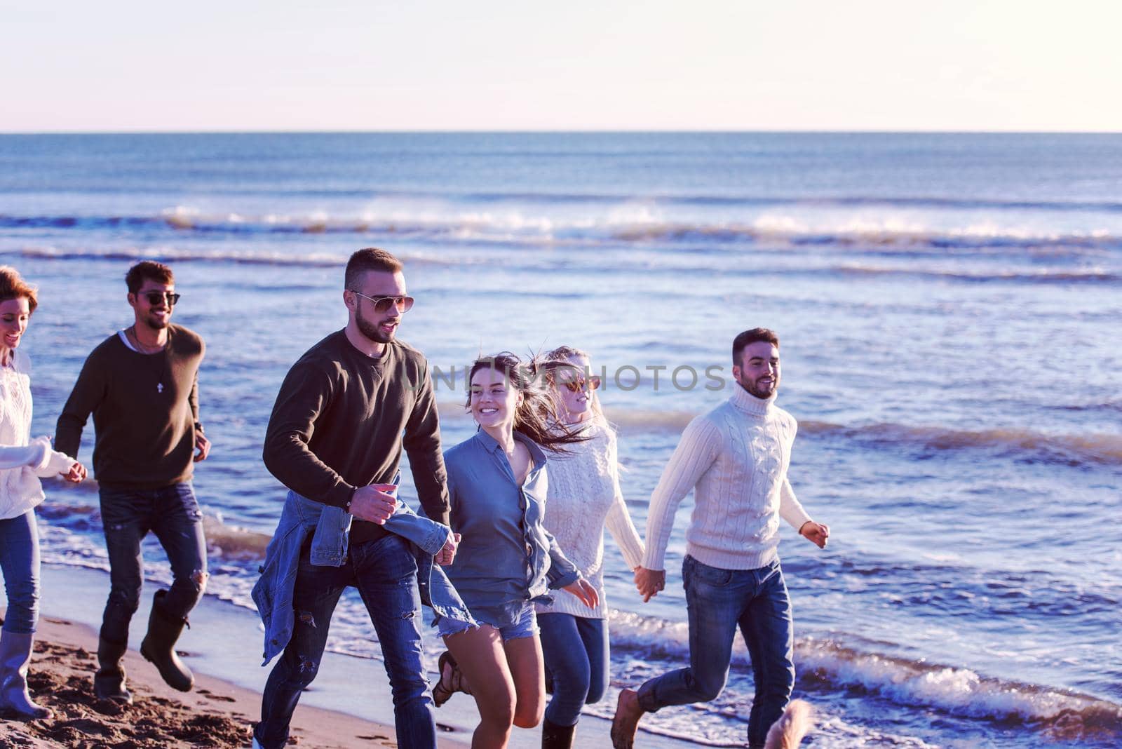 Group of friends running on beach during autumn day by dotshock