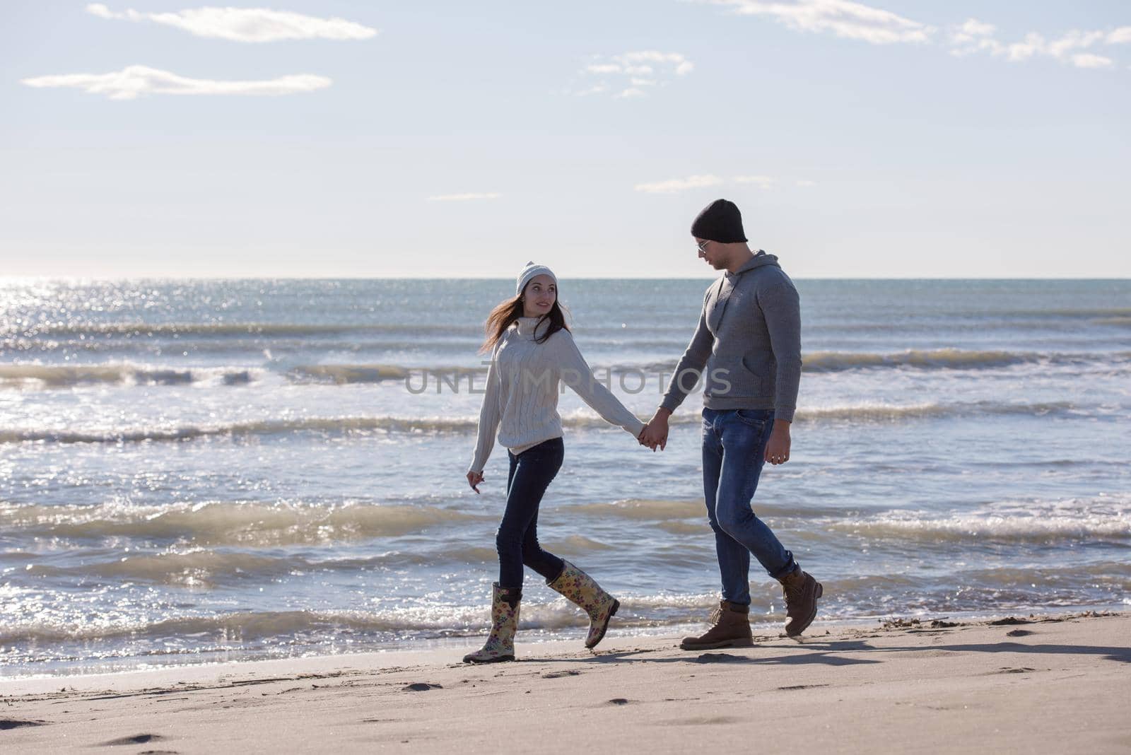 Young couple having fun walking and hugging on beach during autumn sunny day