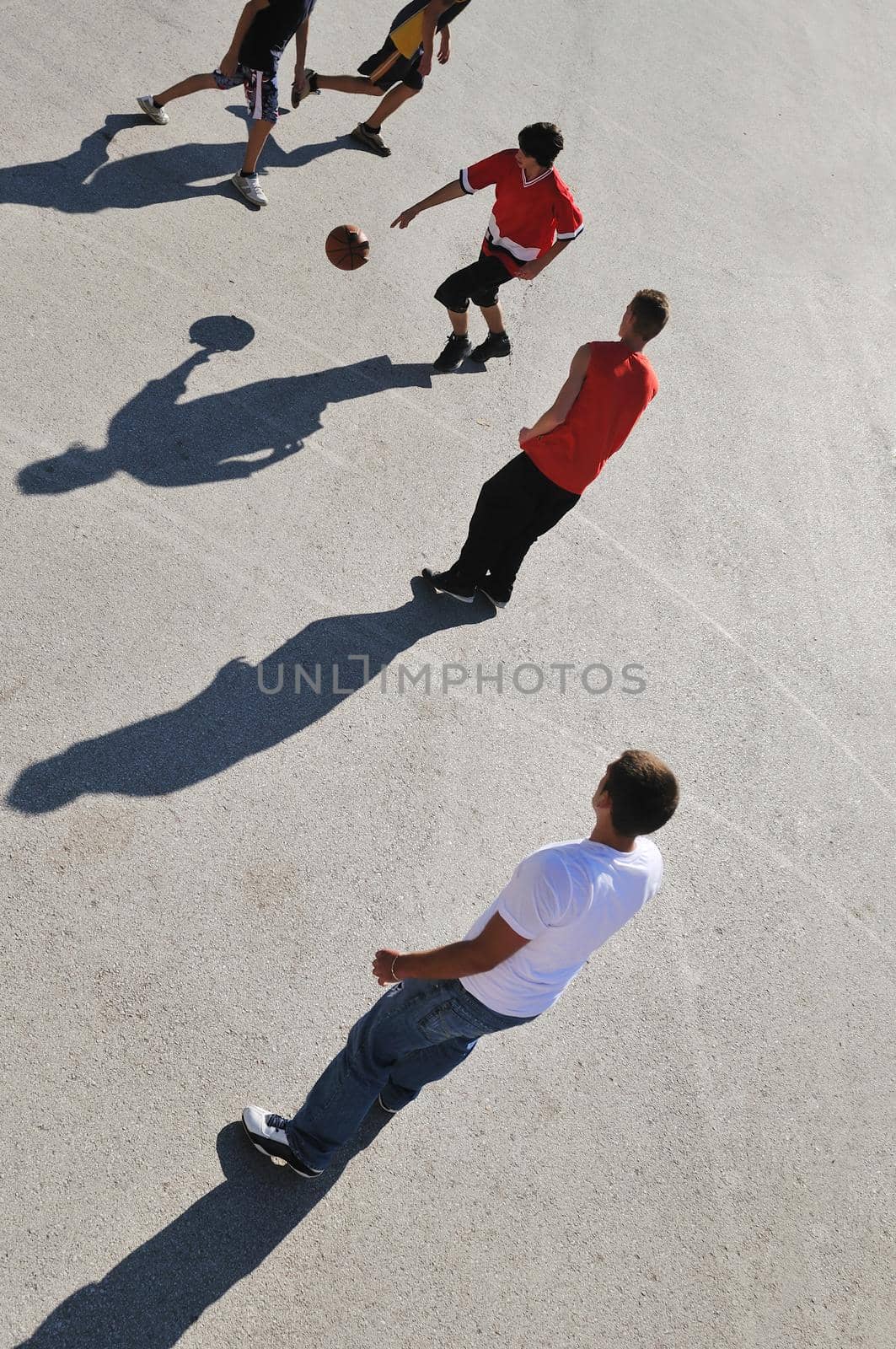 gorup of young boys who playing basketball outdoor on street with long shadows and bird view perspective