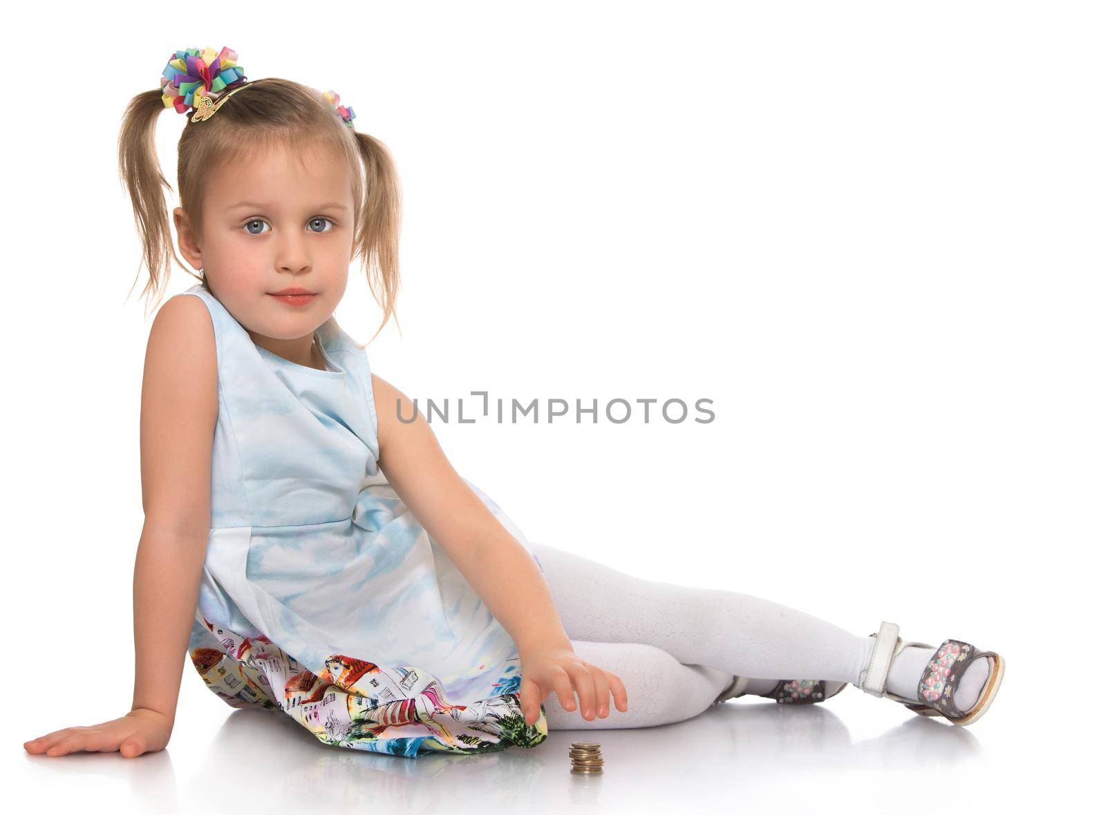 Cute little girl with a long ponytail down to his shoulders . Girl sitting on the floor . She puts a pile of coins - Isolated on white background