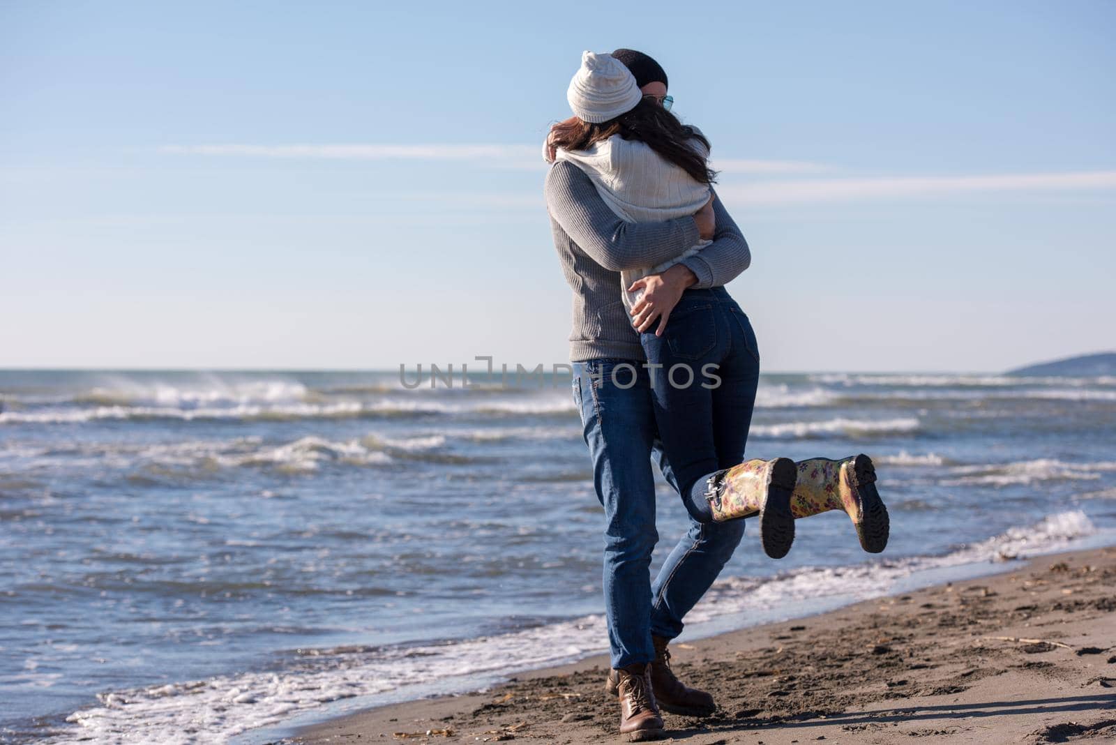 Young couple having fun walking and hugging on beach during autumn sunny day