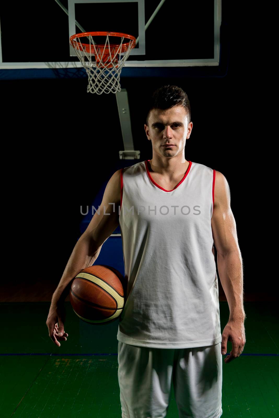 Basketball player portrait  on basketball court holding ball with black isolated background