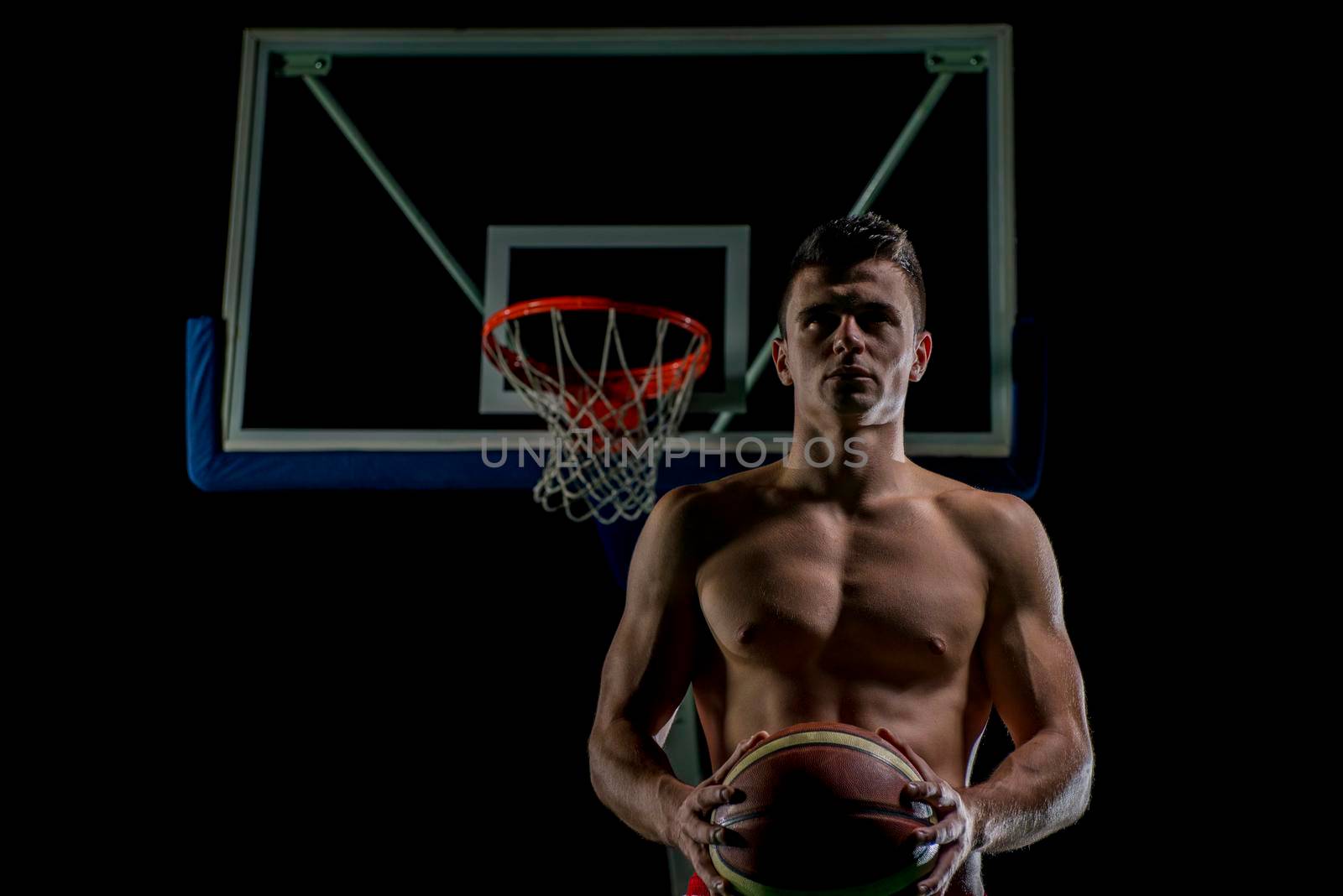 Basketball player portrait  on basketball court holding ball with black isolated background