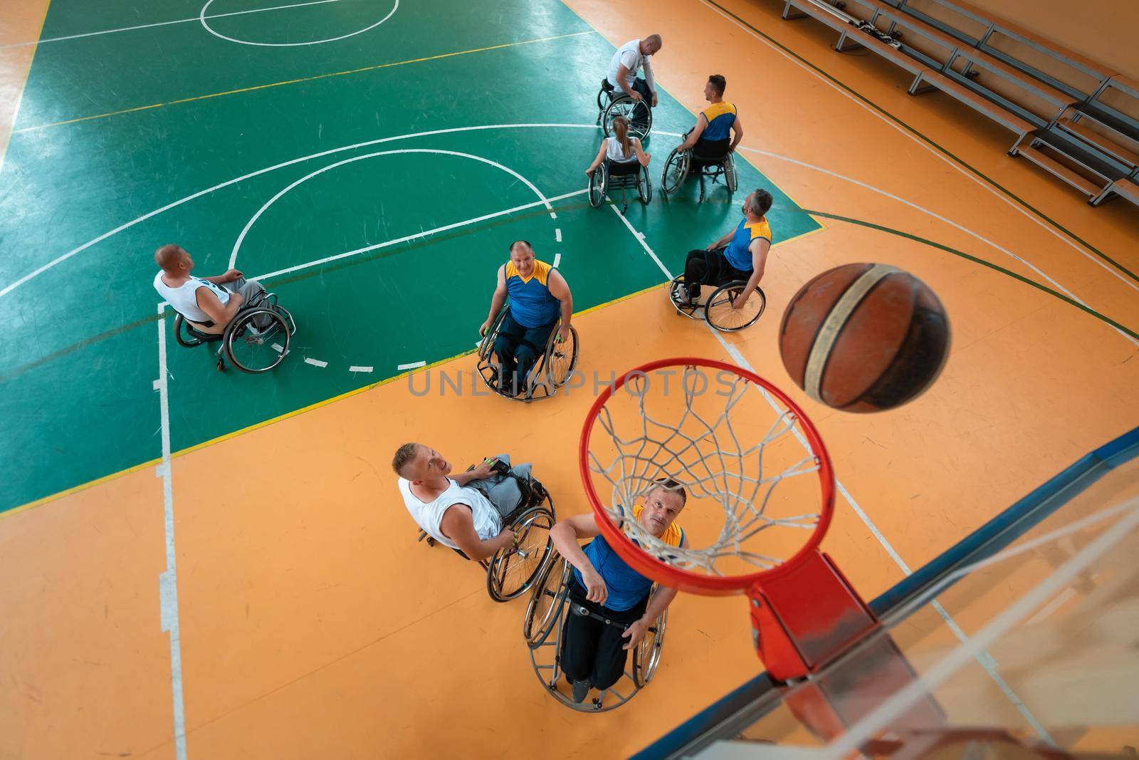 Disabled War or work veterans mixed race and age basketball teams in wheelchairs playing a training match in a sports gym hall. Handicapped people rehabilitation and inclusion concept.  by dotshock