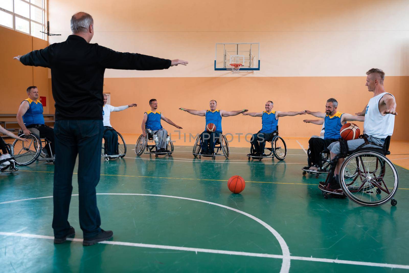 the selector of the basketball team with a disability stands in front of the players and shows them the stretching exercises before the start of training by dotshock