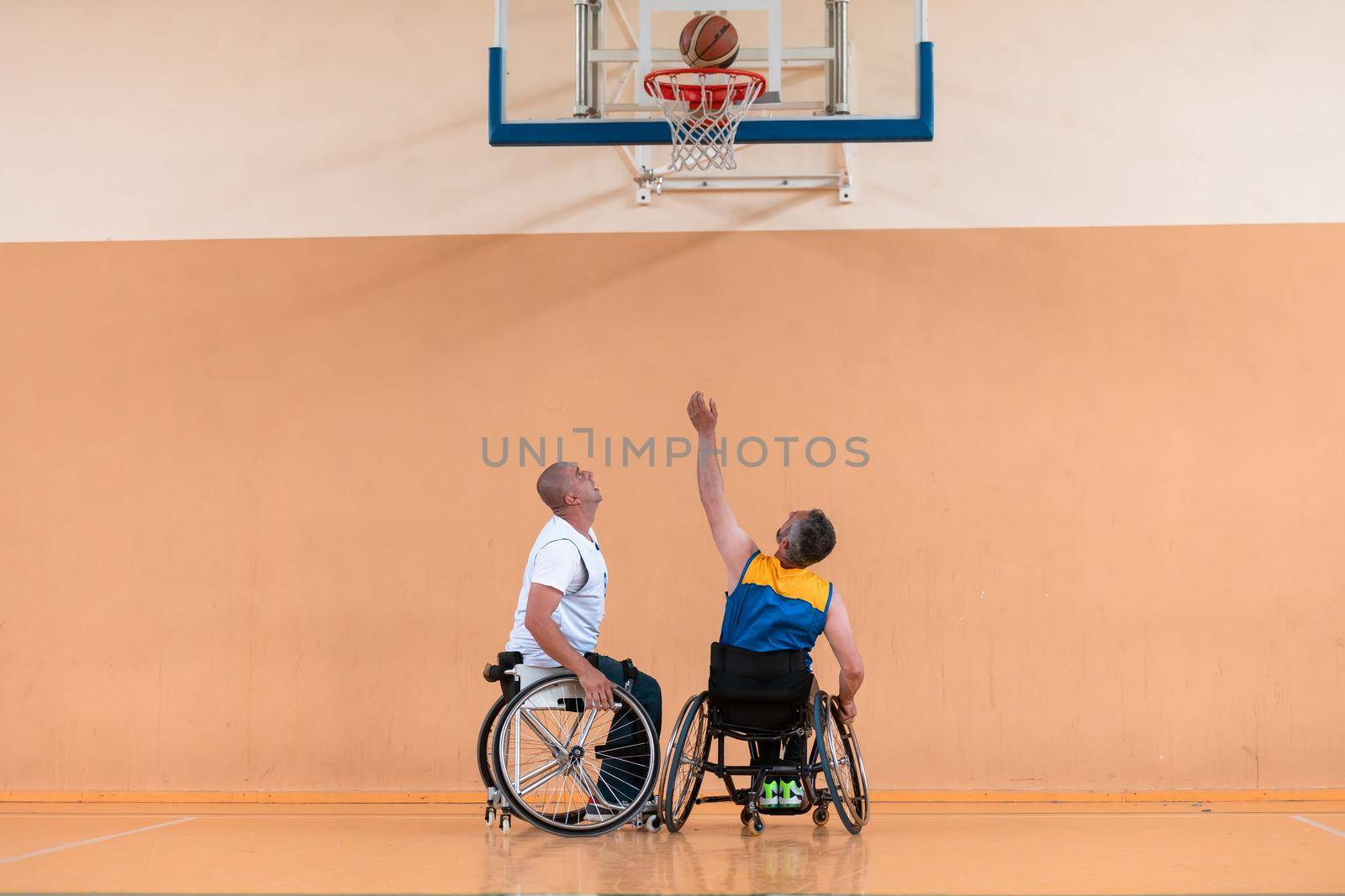 Disabled War veterans mixed race and age basketball teams in wheelchairs playing a training match in a sports gym hall. Handicapped people rehabilitation and inclusion concept by dotshock