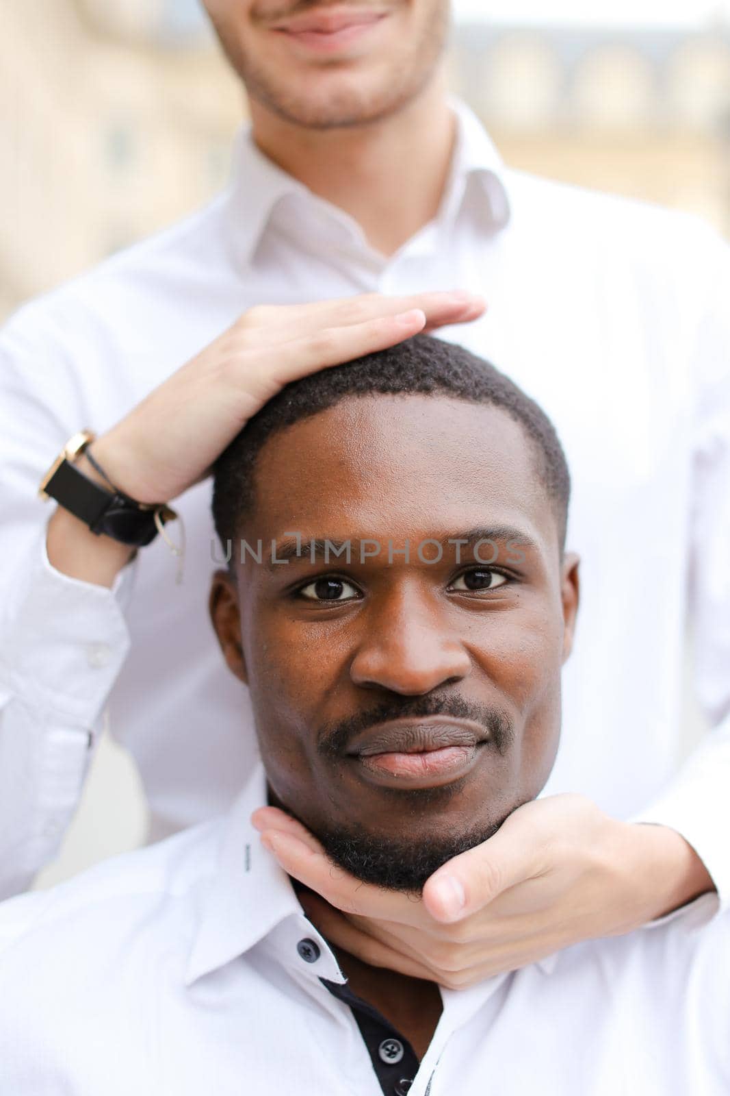 Caucasian man holding afro american guy head by hands.