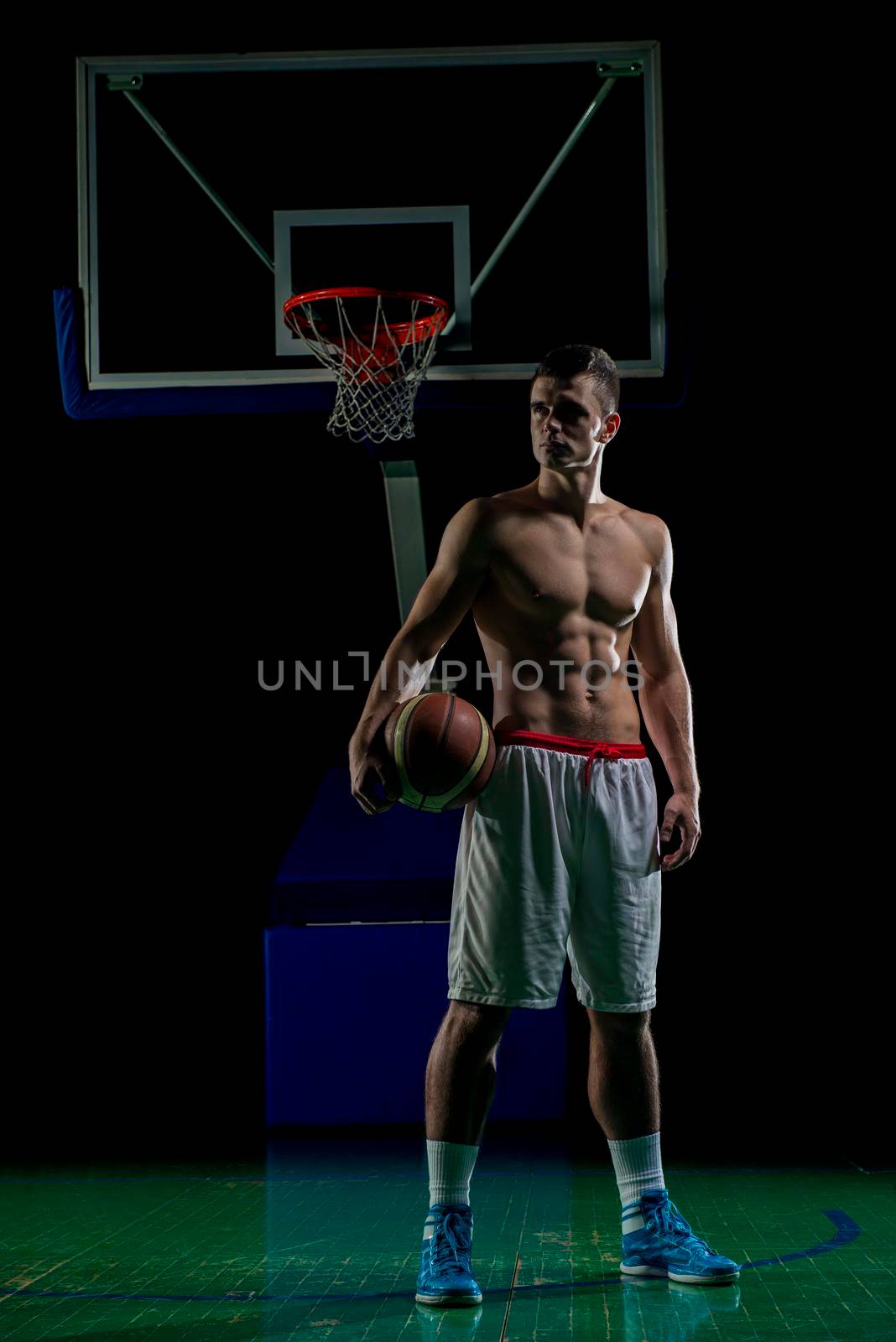 Basketball player portrait  on basketball court holding ball with black isolated background