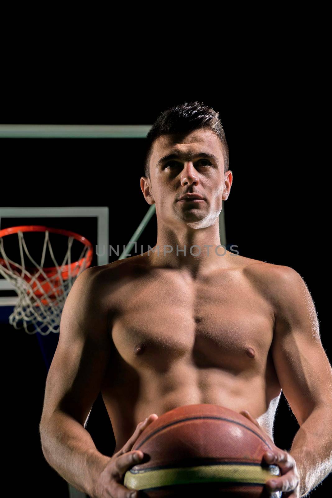 Basketball player portrait  on basketball court holding ball with black isolated background