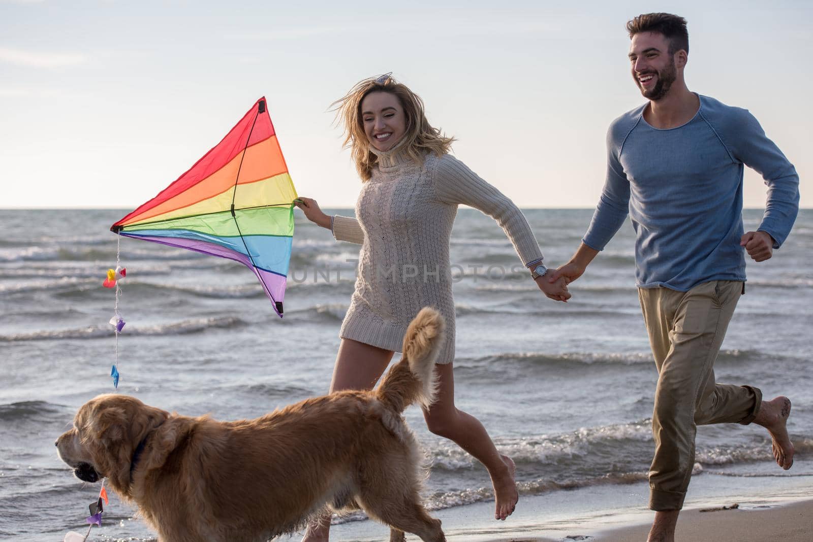 Young Couple having fun playing with a dog and Kite on the beach at autumn day