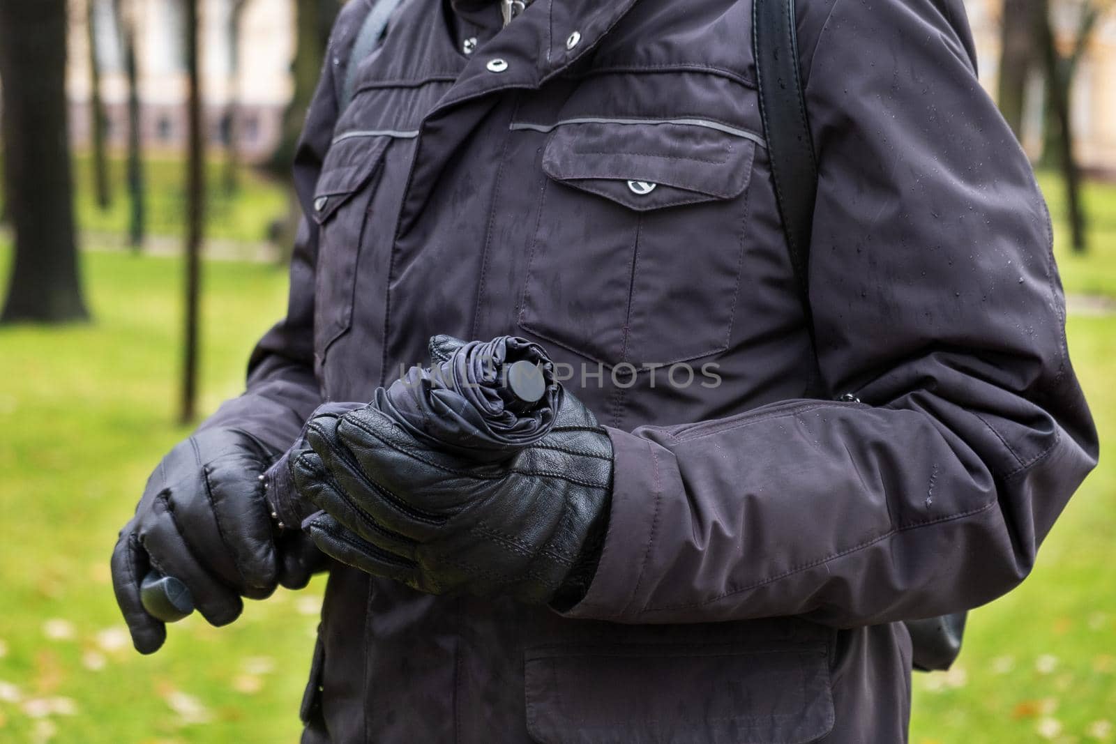 Close-up of man's hand in jacket and gloves holding closed umbrella by OlgaGubskaya